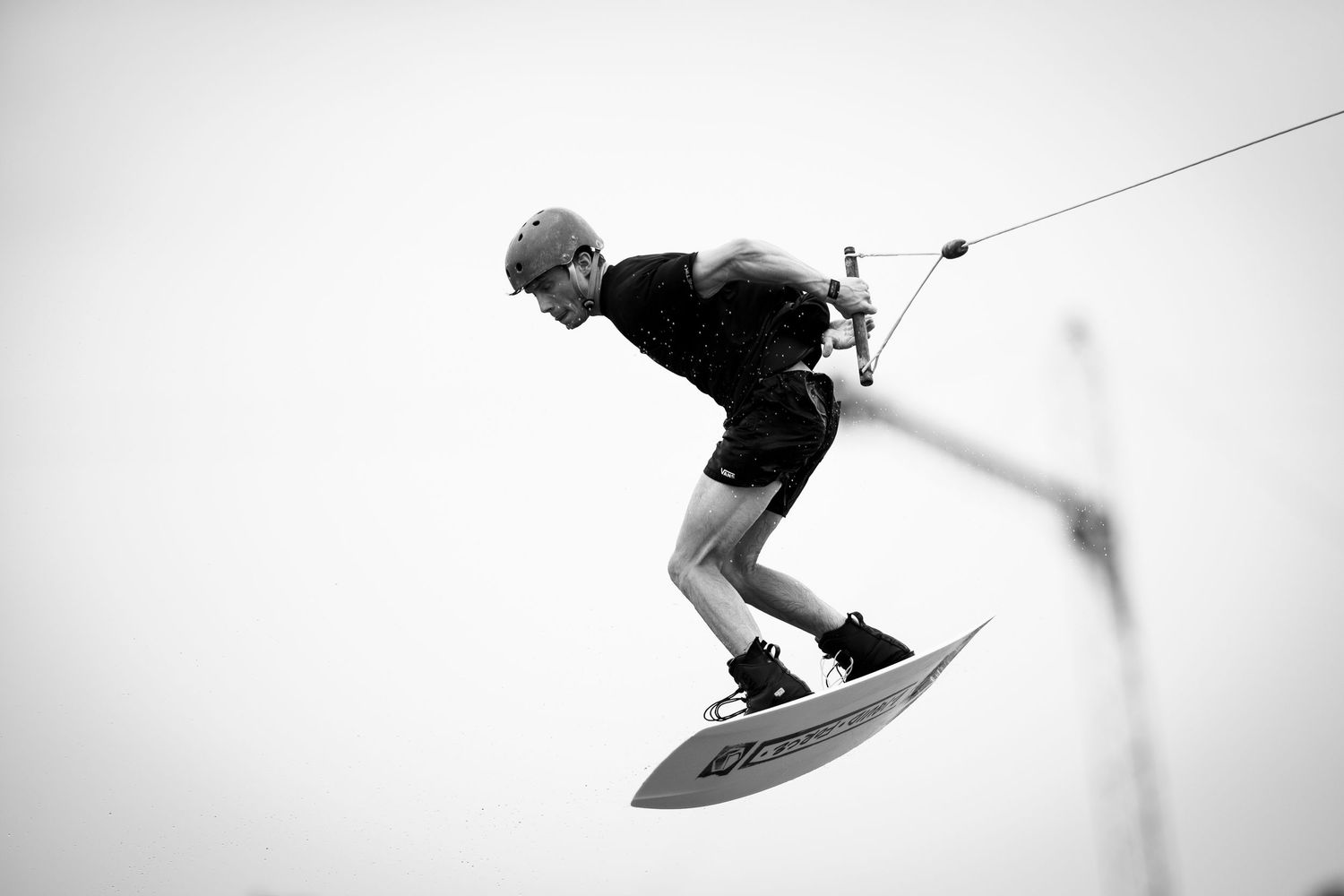 Black and white shot of wakeboarder performing aerial maneuver against bright sky.