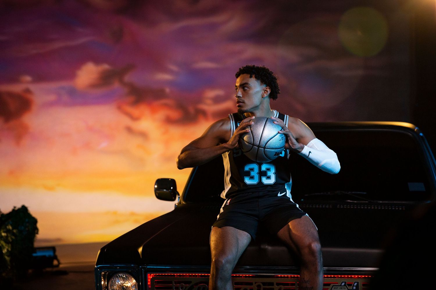 Basketball player wearing number 33 poses dramatically against a sunset backdrop.