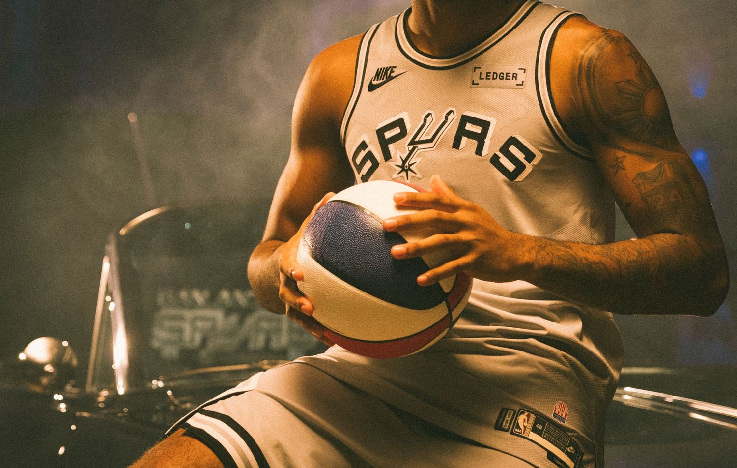 San Antonio Spurs NBA player holding basketball in Nike jersey under dramatic studio lighting.