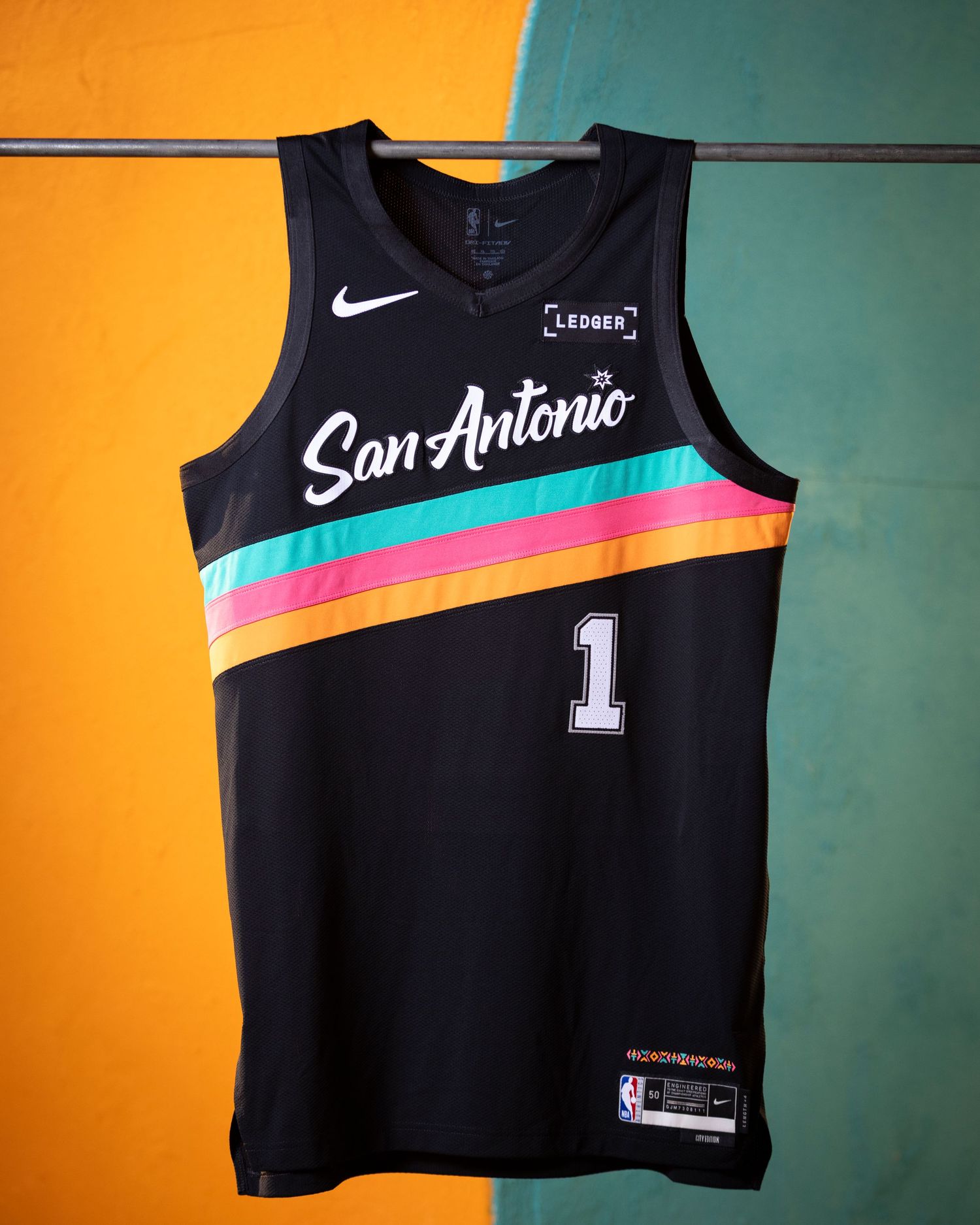 Nike San Antonio Spurs black city edition jersey number 1 hanging against colorful teal and yellow wall.