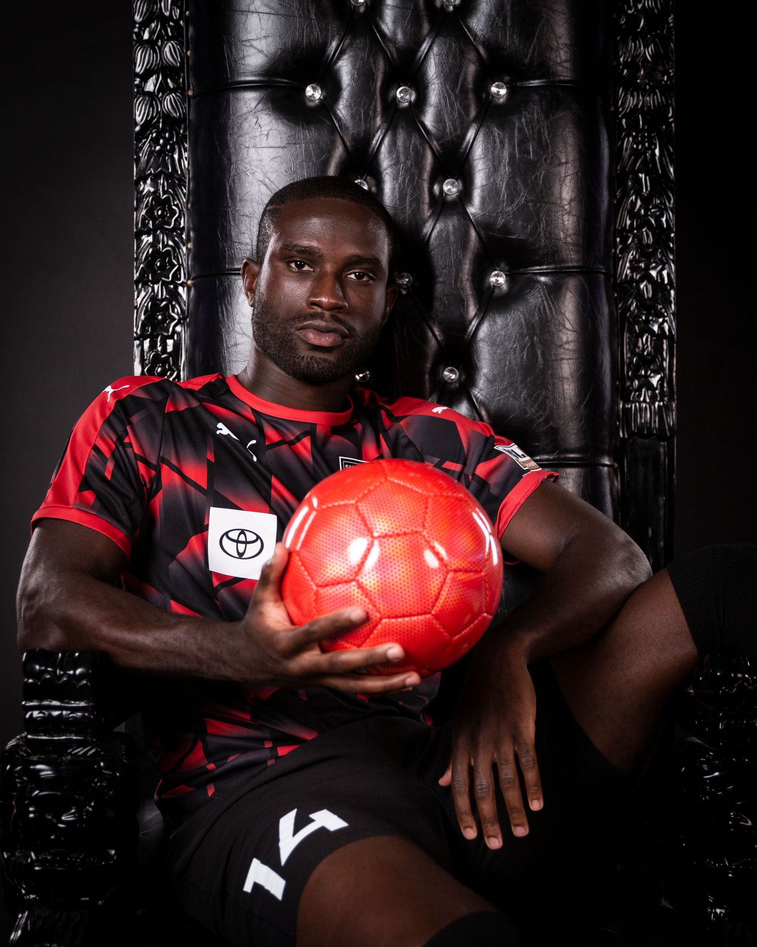 Athlete poses with red soccer ball in black throne wearing San Antonio FC jersey.