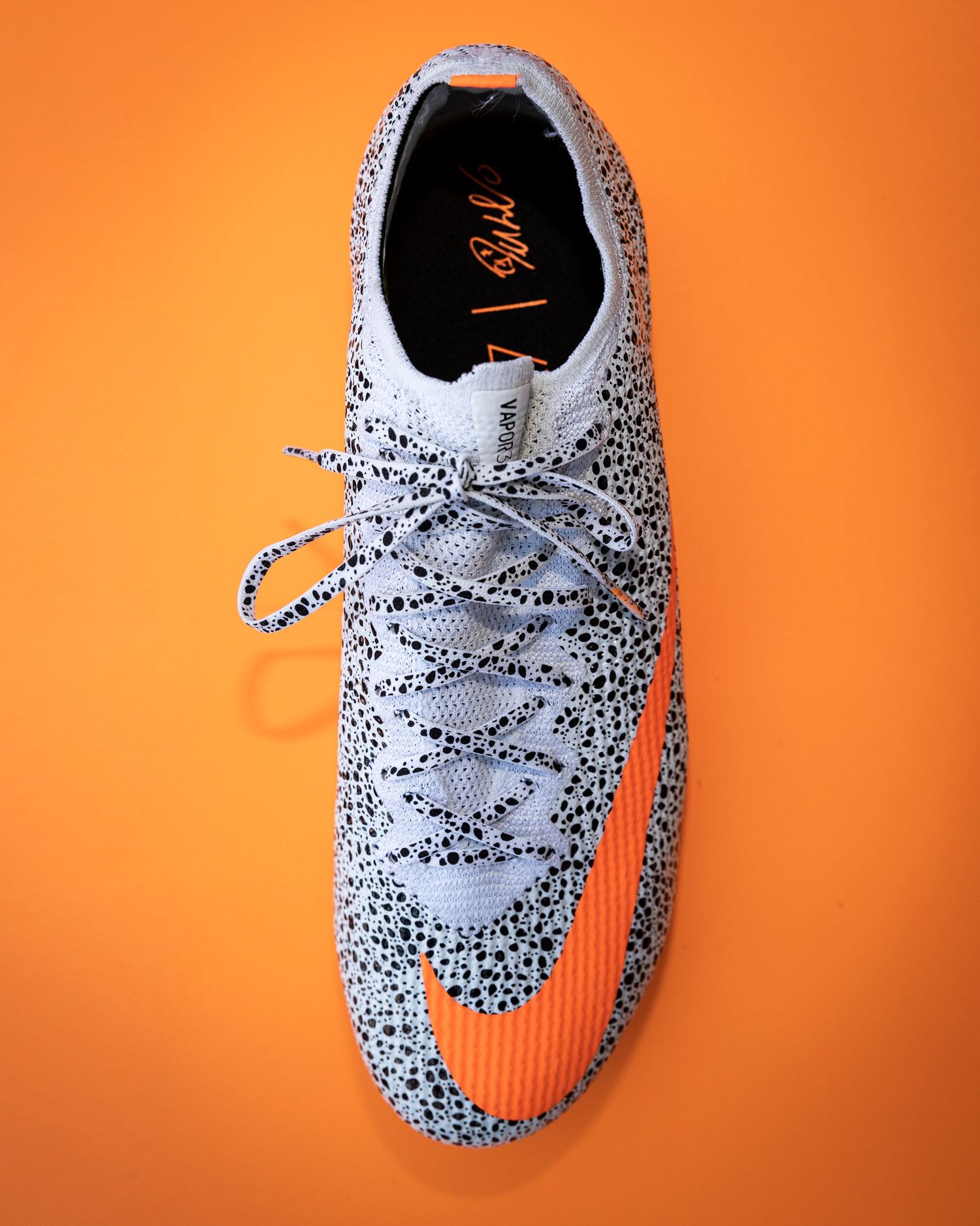 White soccer cleats with spotted pattern showcased on bright orange surface.