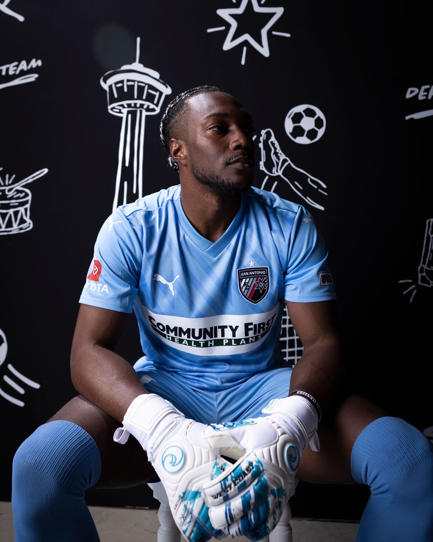 Soccer player in light blue uniform sits against wall with illustrated sports icons.