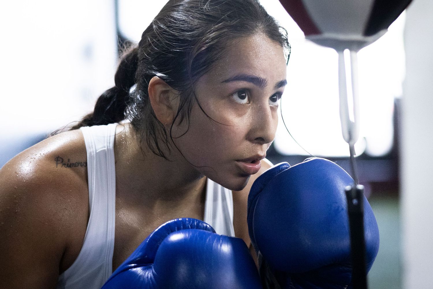 Boxer in white tank top with blue gloves in defensive stance during training.