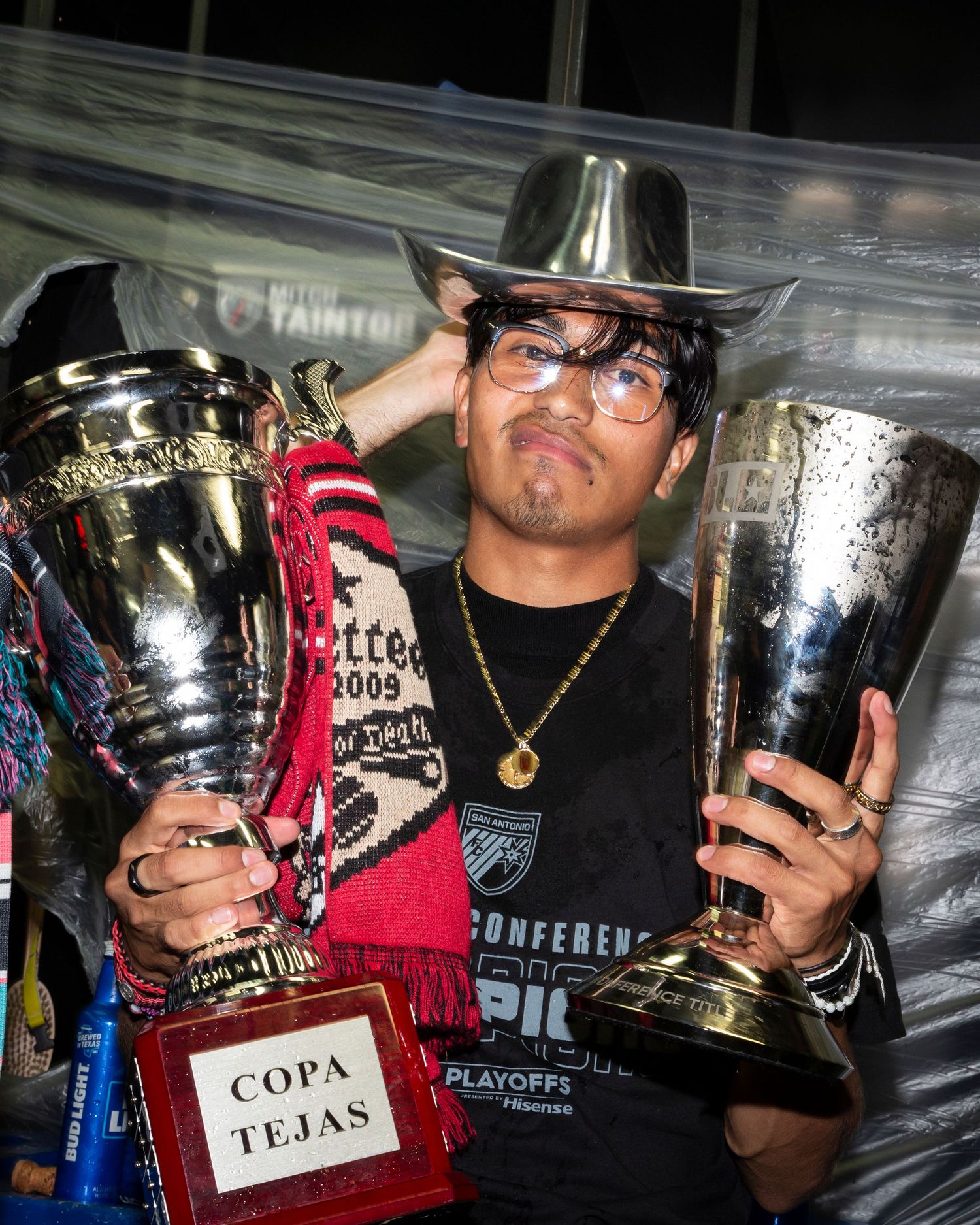 Player holding two championship trophies including Copa Tejas while wearing a cowboy hat.
