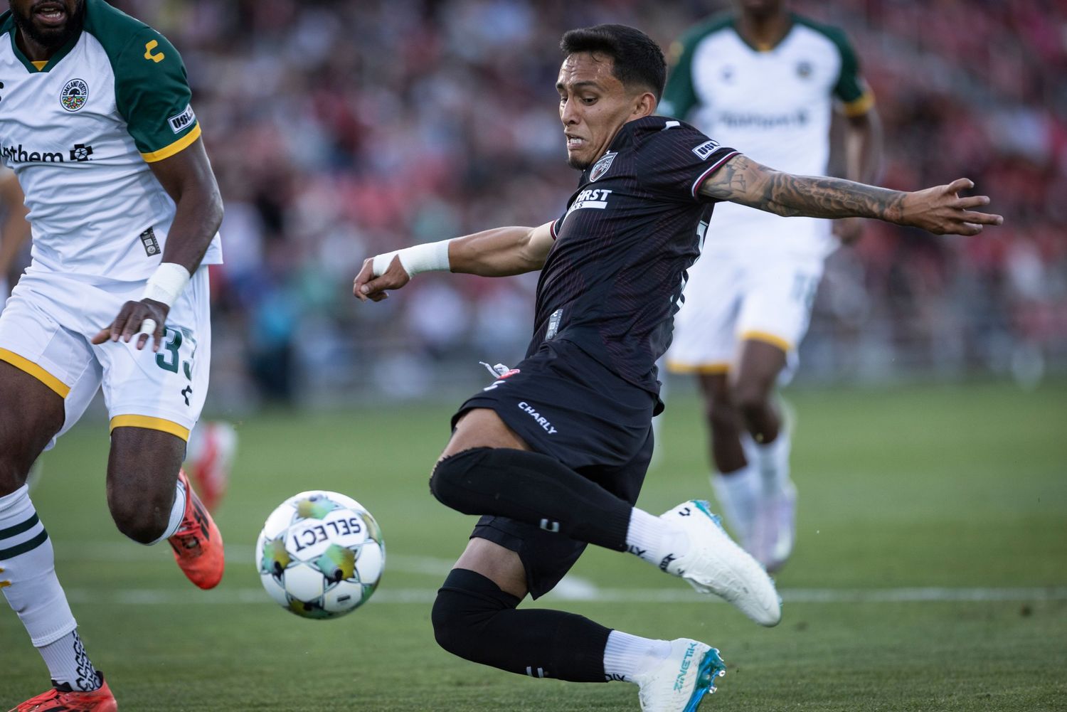 Soccer player in black uniform stretches to control the ball during game action.