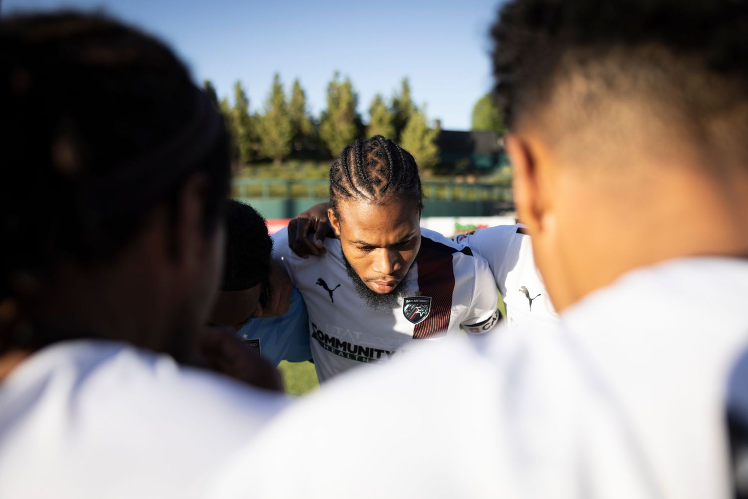 Athletes huddle together during a pre-game team meeting outdoors.