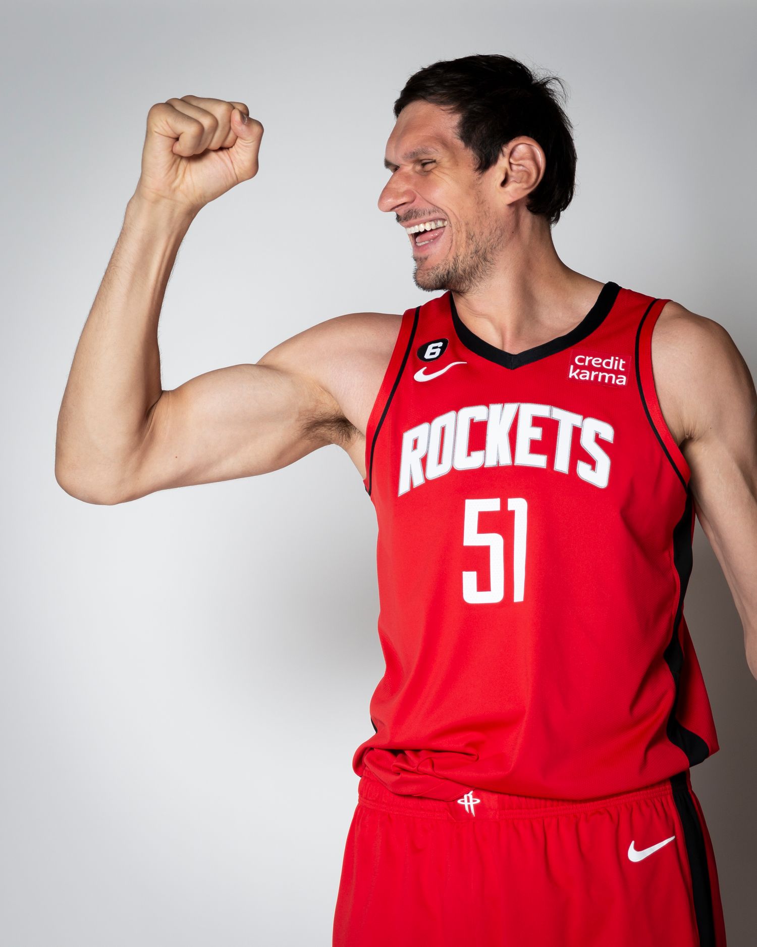 Professional basketball player in red Rockets jersey flexing arm in celebratory pose.