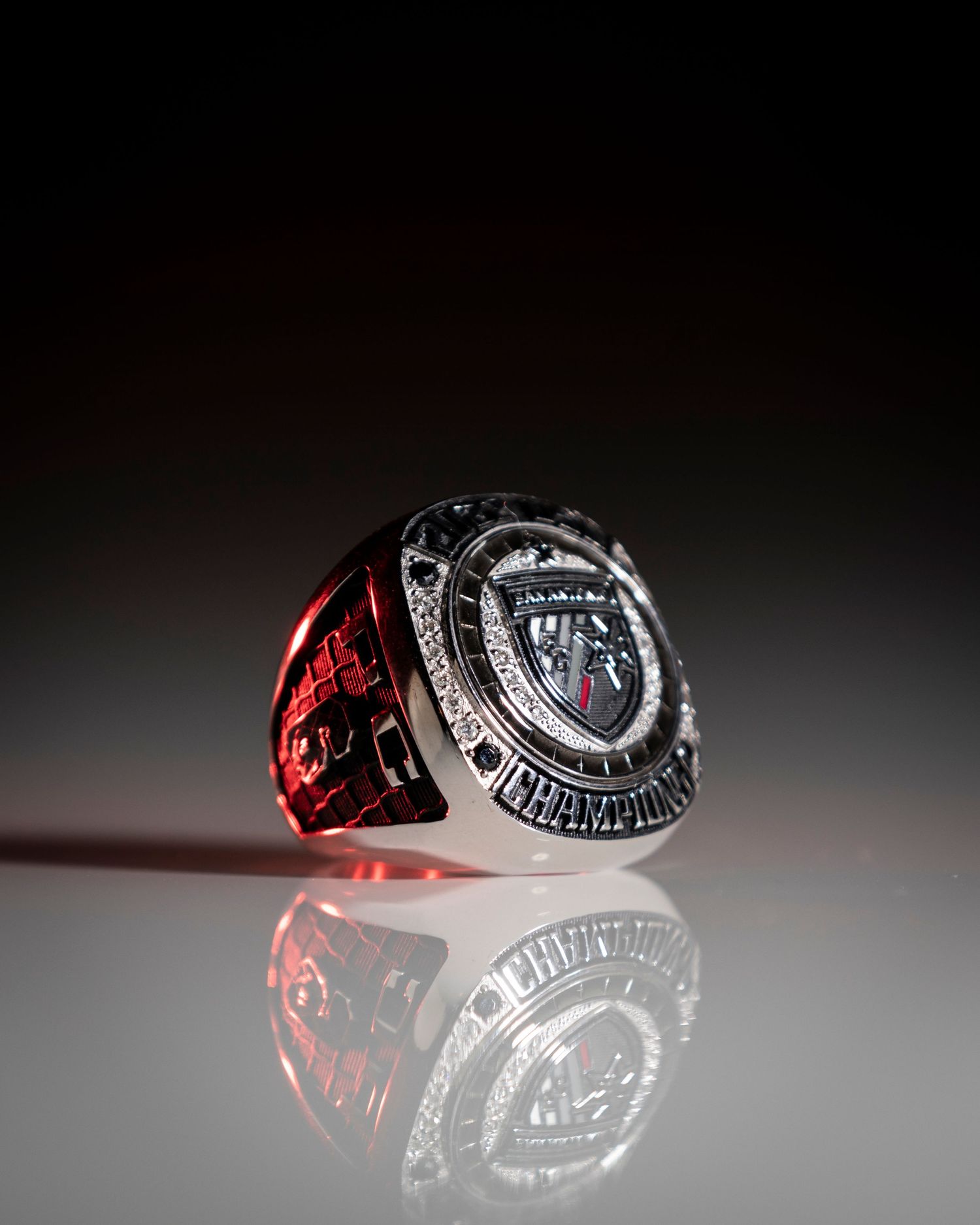 Championship ring photographed with dramatic lighting and reflective surface.