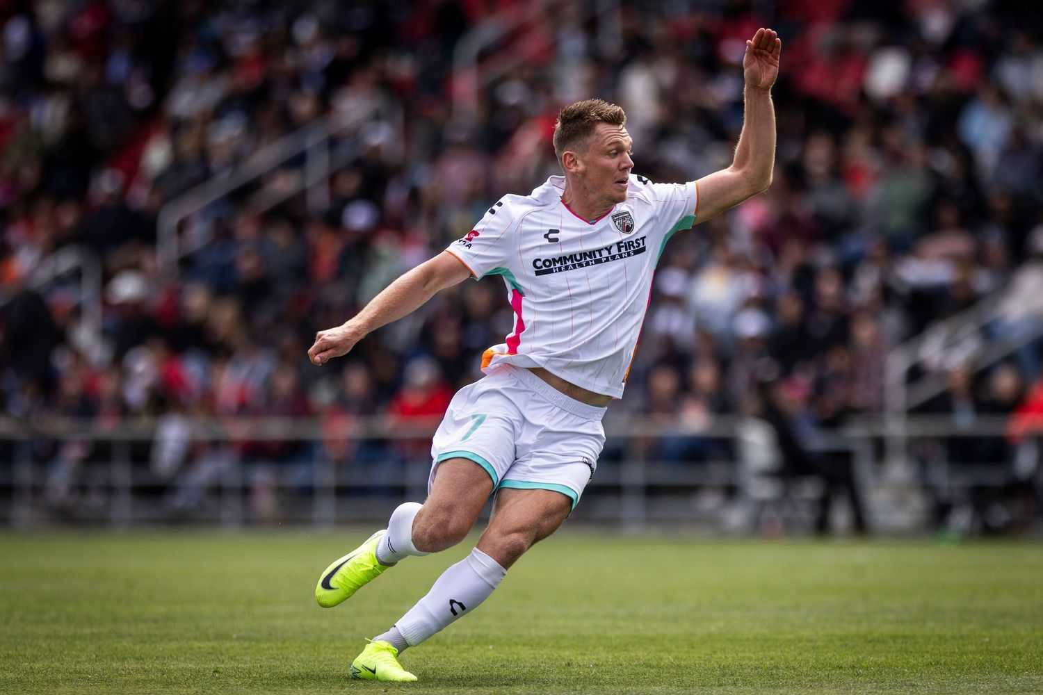 Soccer player in white uniform leaps with outstretched arm during match action.