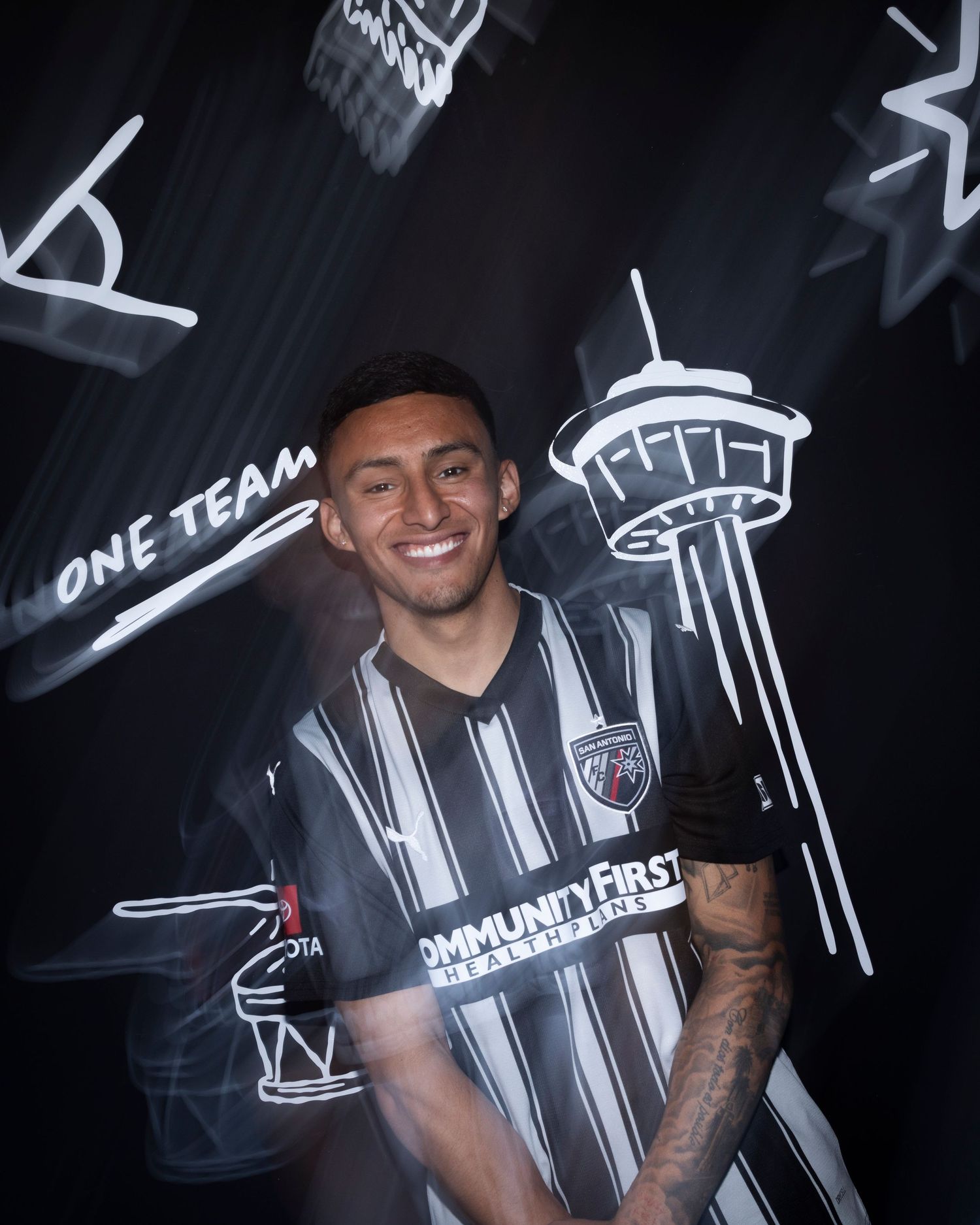 Soccer player in black and white striped jersey poses with Space Needle doodle art background.