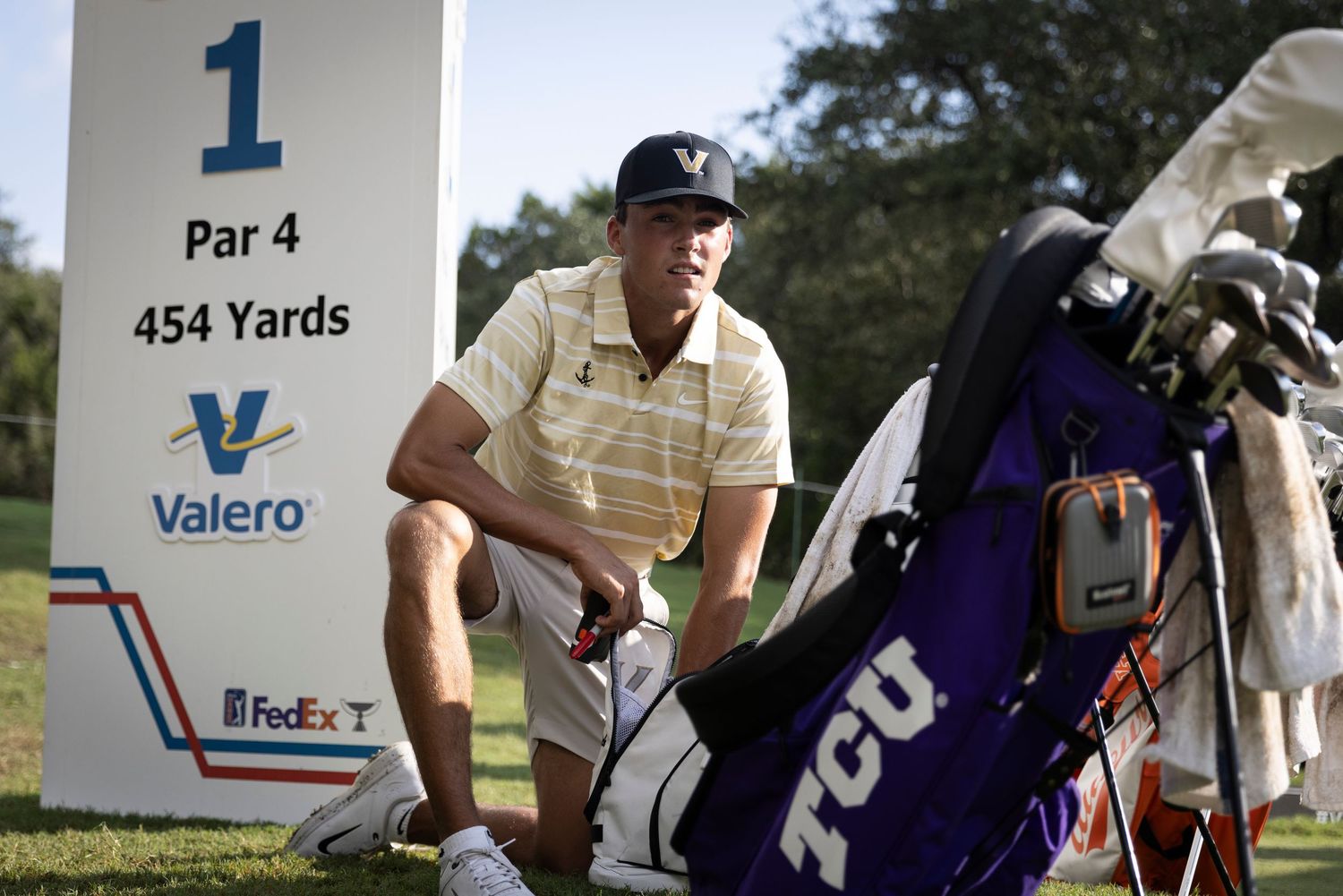 Golfer crouching to read green at first hole with golf bag and tee marker visible.