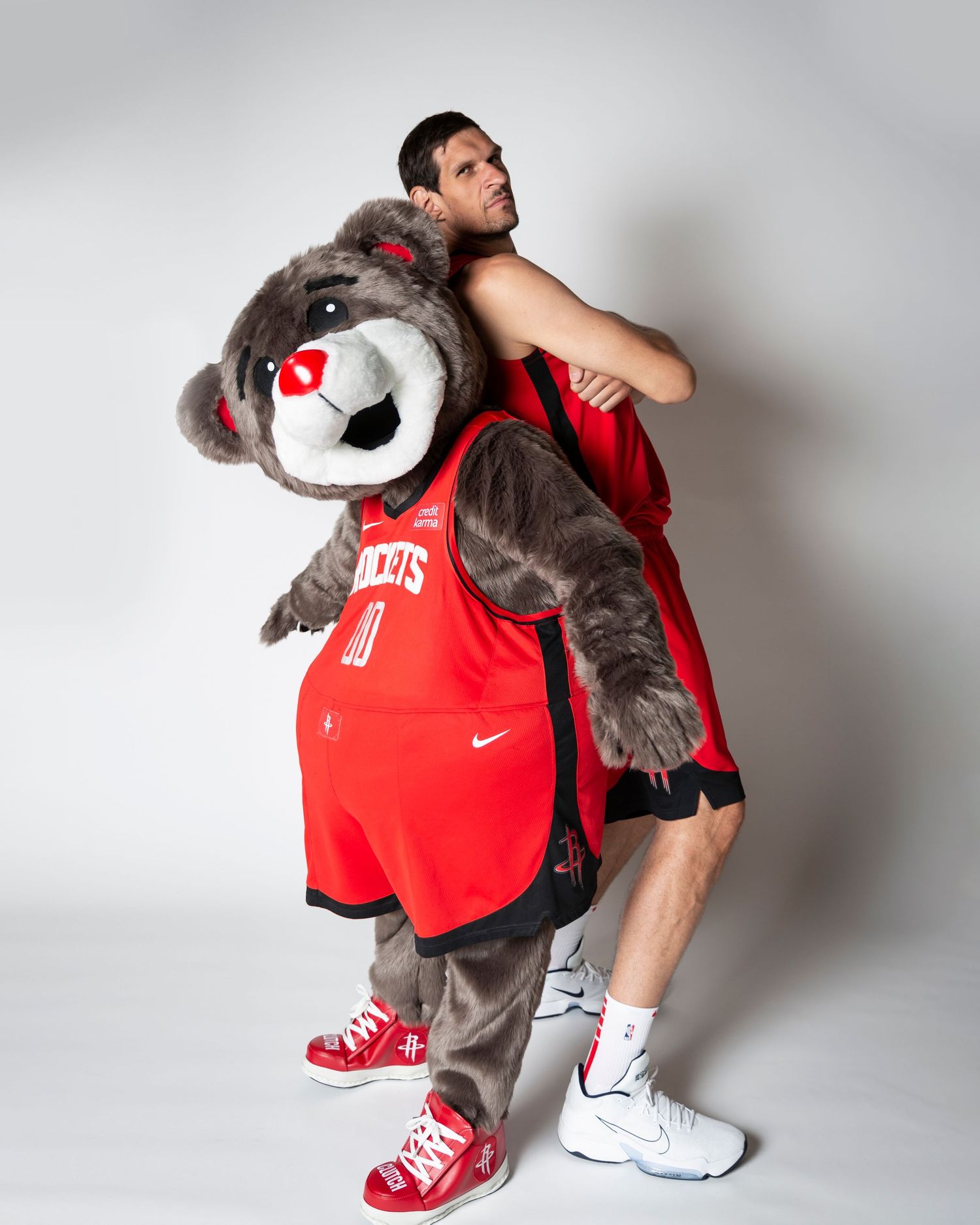 NBA mascot in Rockets uniform poses back-to-back with player during team photoshoot.