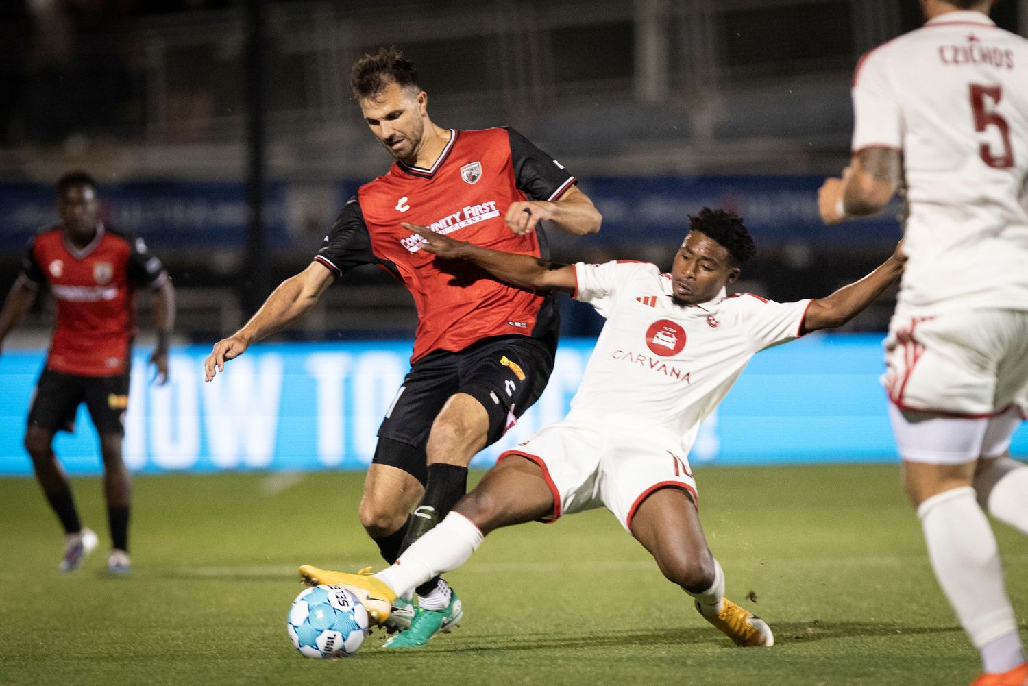 Two soccer players battle for ball during competitive night match on outdoor pitch.