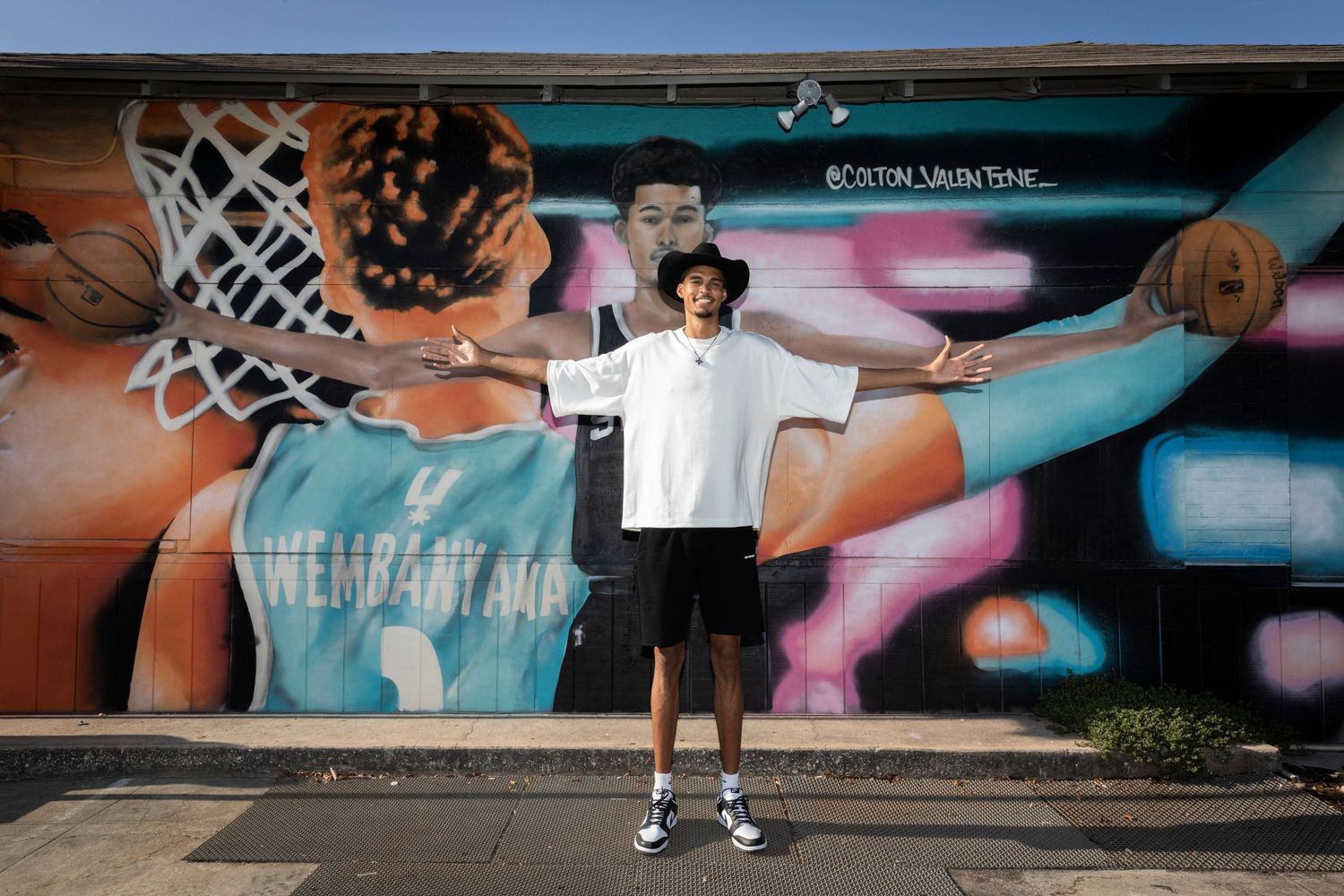 Person standing with arms spread wide in front of colorful basketball-themed mural.