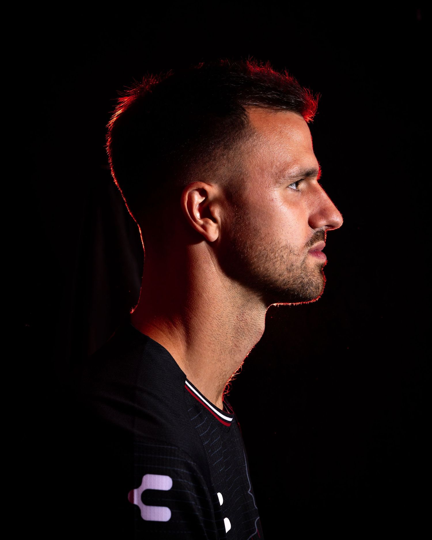 Side profile portrait of athletic figure in black jersey with dramatic red lighting effect.