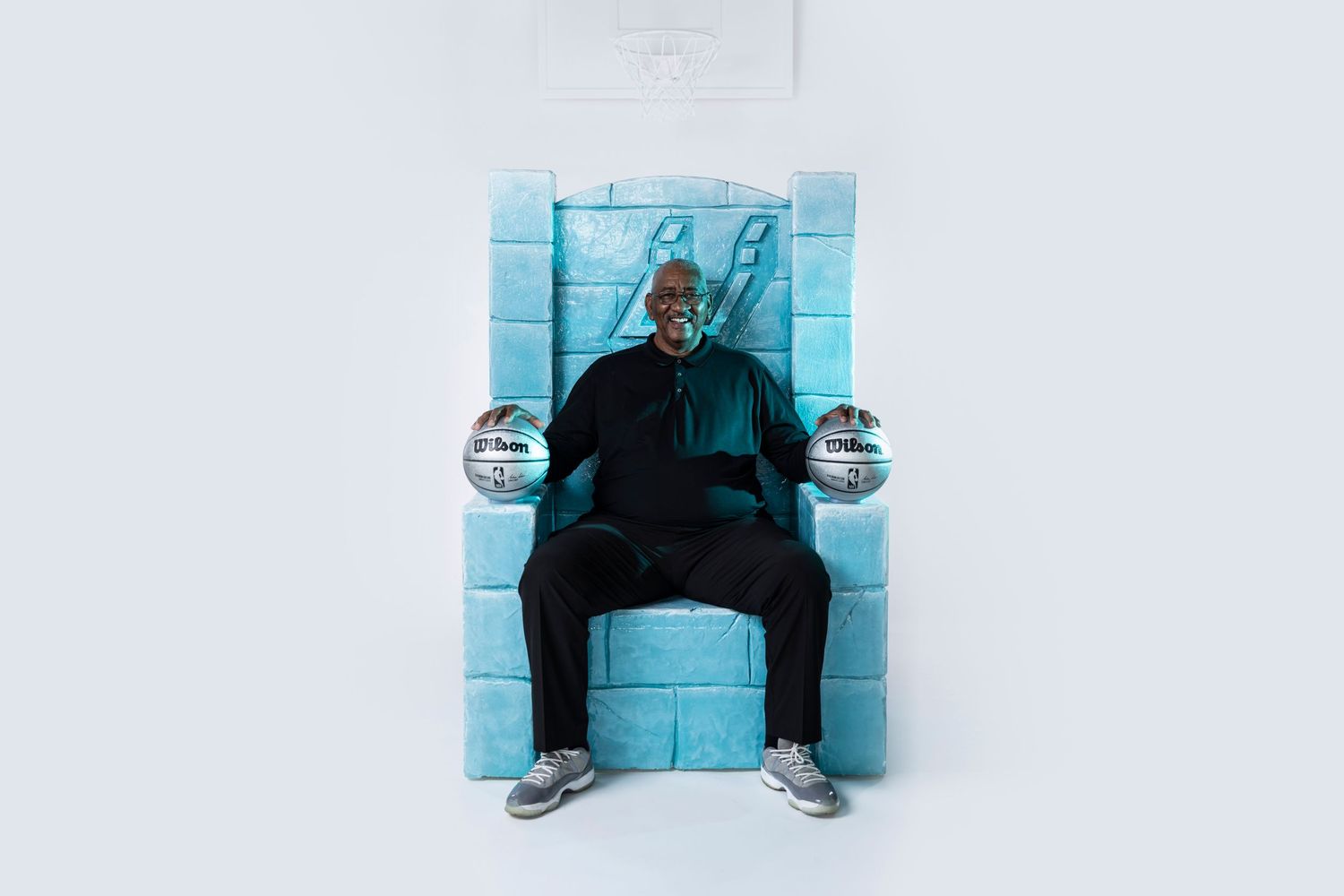Person seated against blue wall holding two crystal balls in artistic portrait.