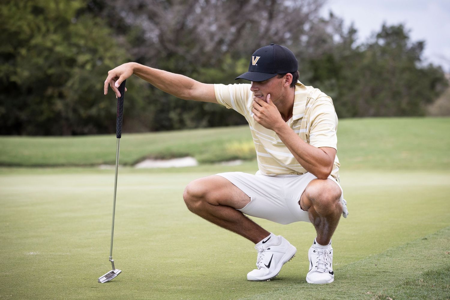 Golfer crouches to analyze putting green while holding putter.