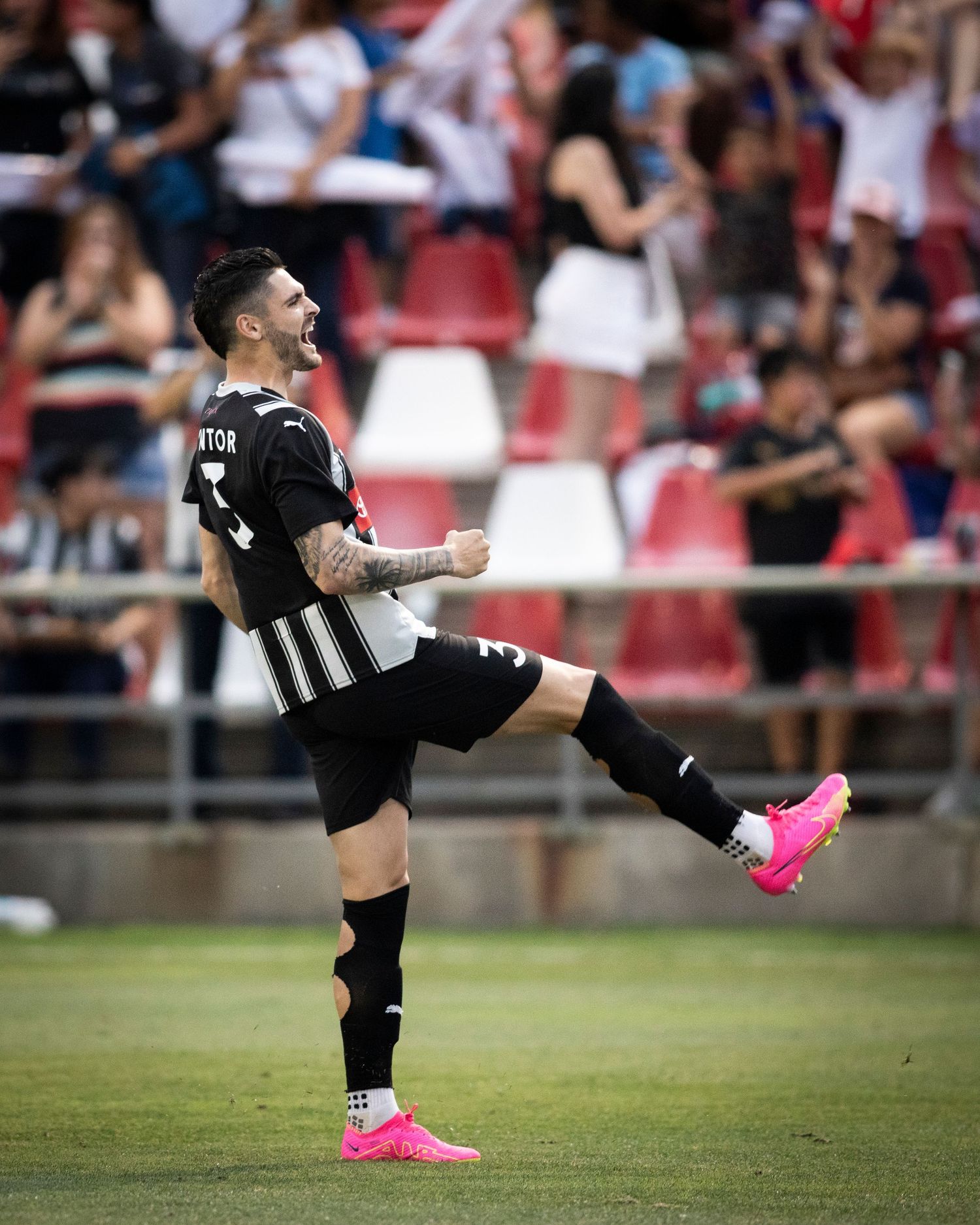 Soccer player in black and white striped uniform kicks leg high during celebration.