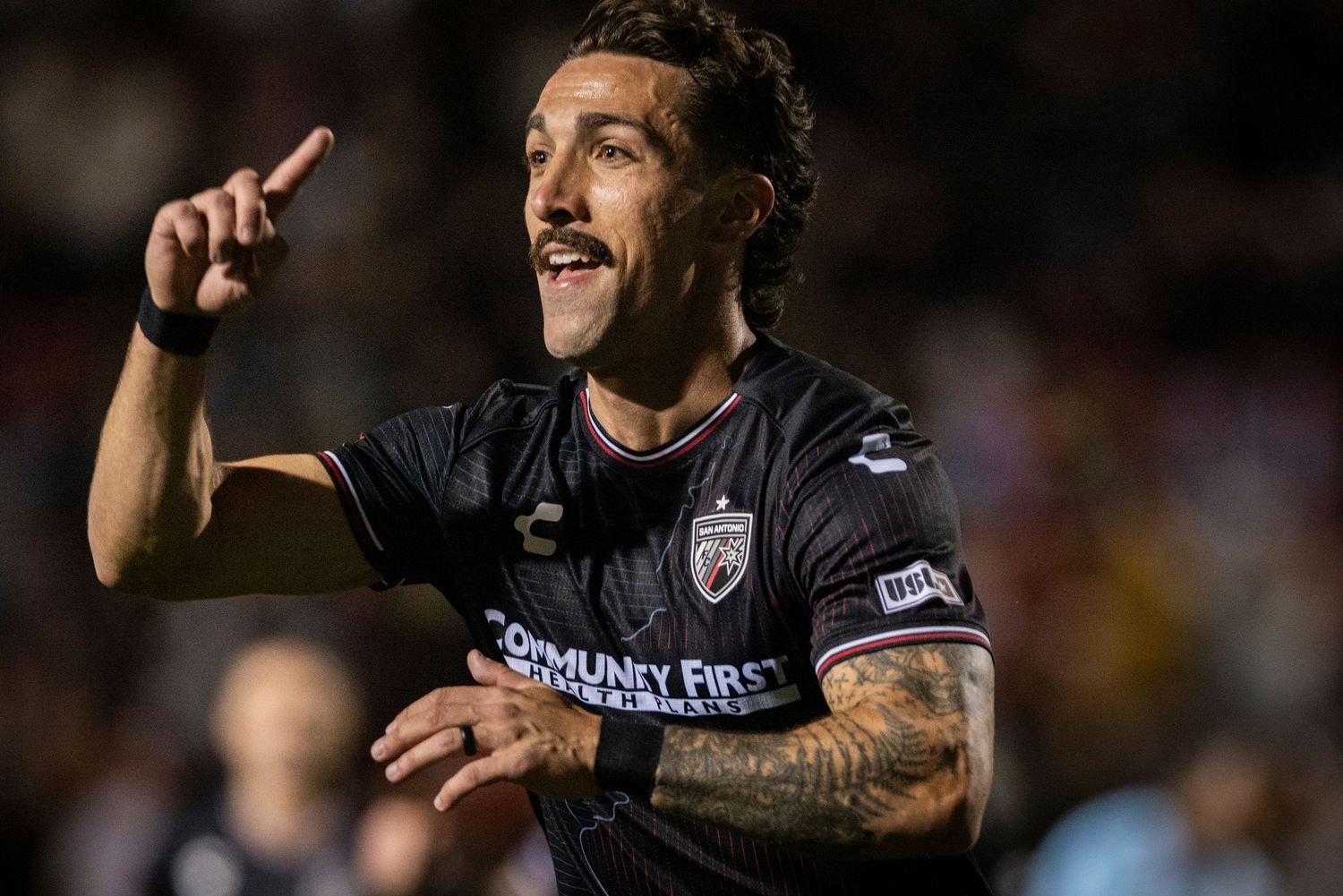 Soccer player in black jersey gestures during celebration at night game.