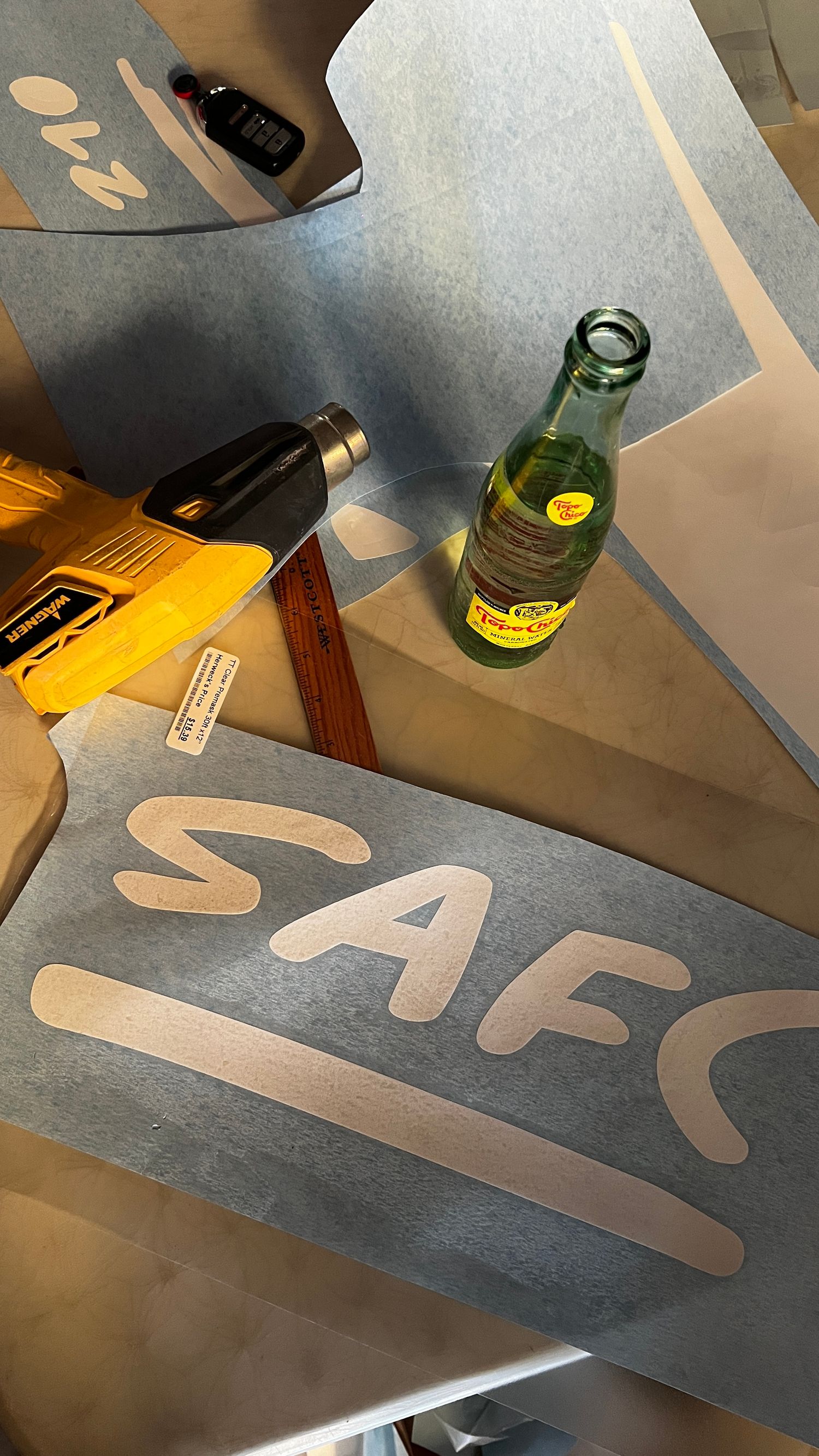 Artistic lettering and typography displayed on a dark surface with glass bottles and objects in the background.