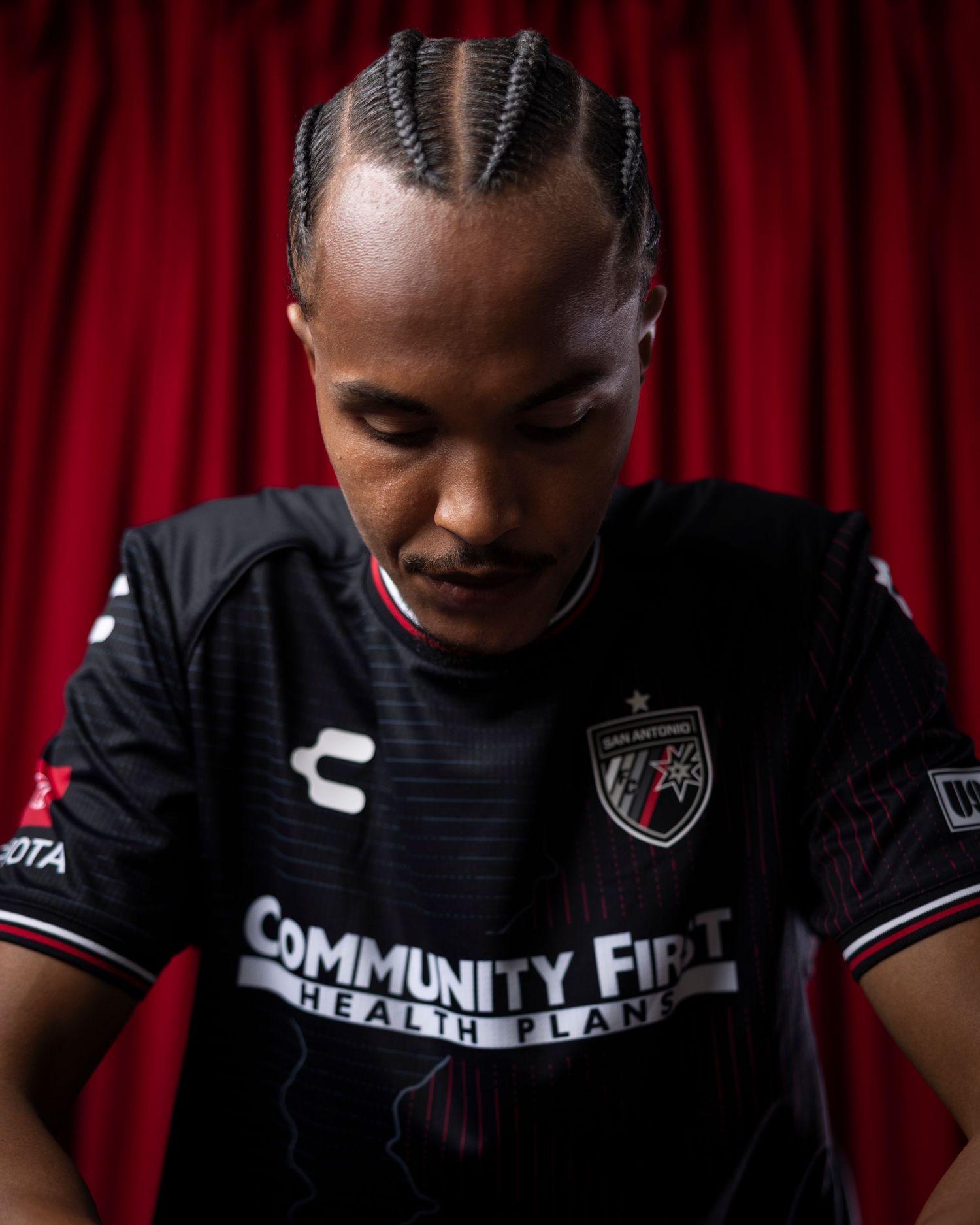 Professional athlete with braided hair looks down wearing black team uniform.