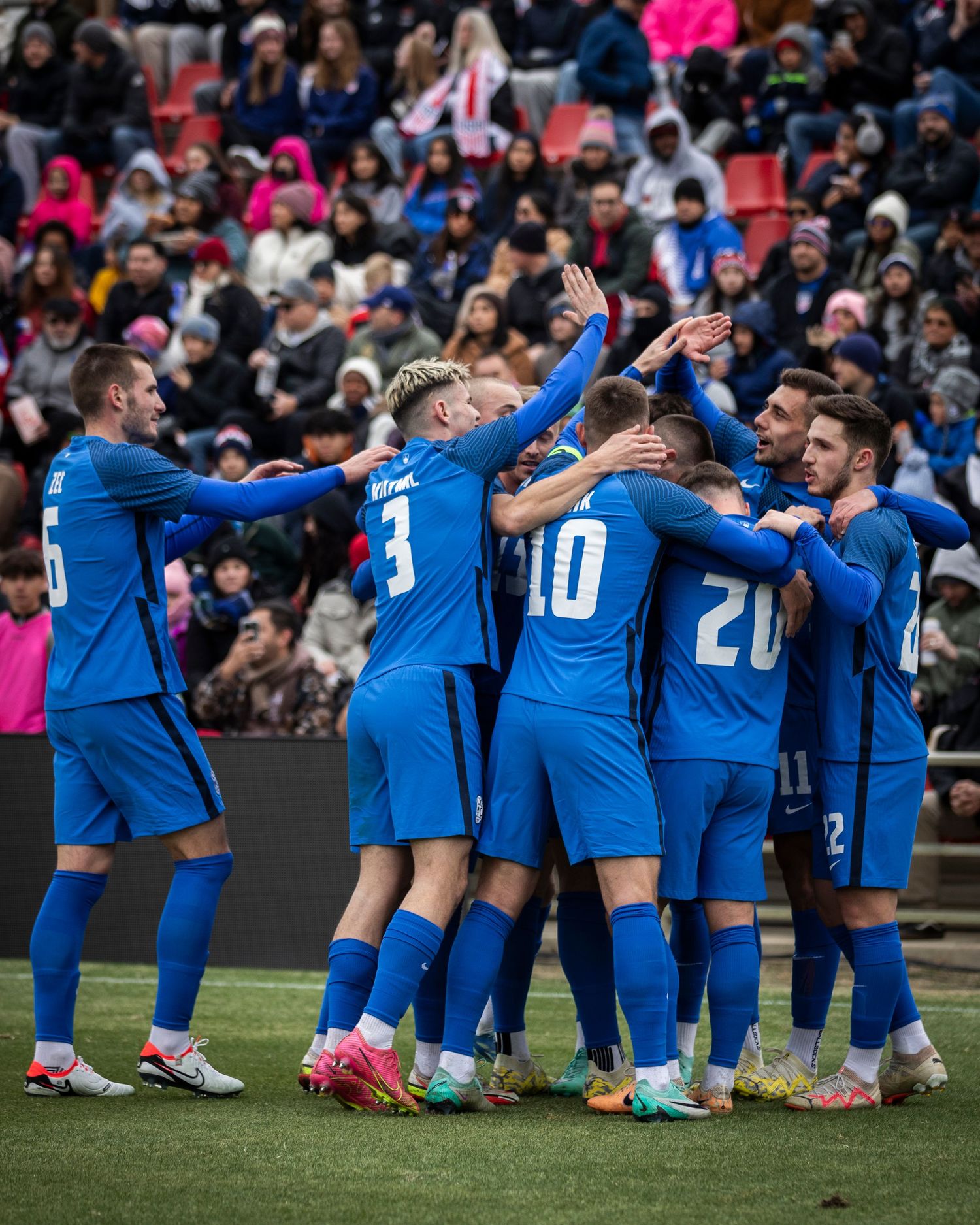 Soccer players in blue uniforms celebrate together on the field during a match.
