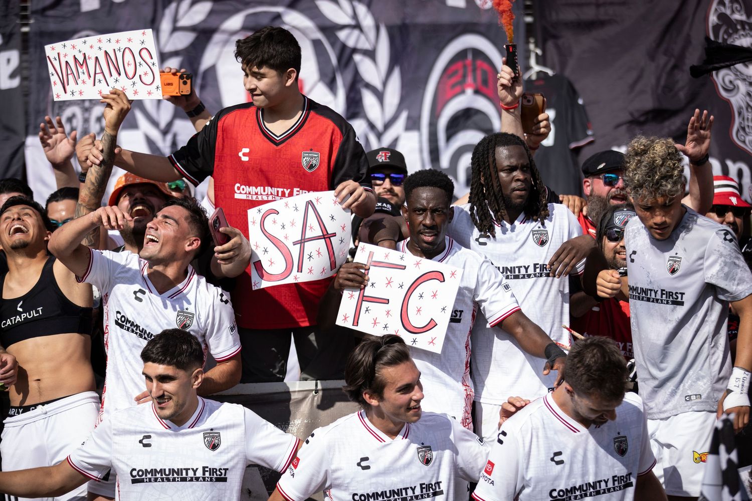 San Antonio FC players and fans celebrate together holding SAFC letters sign after a winning soccer match.