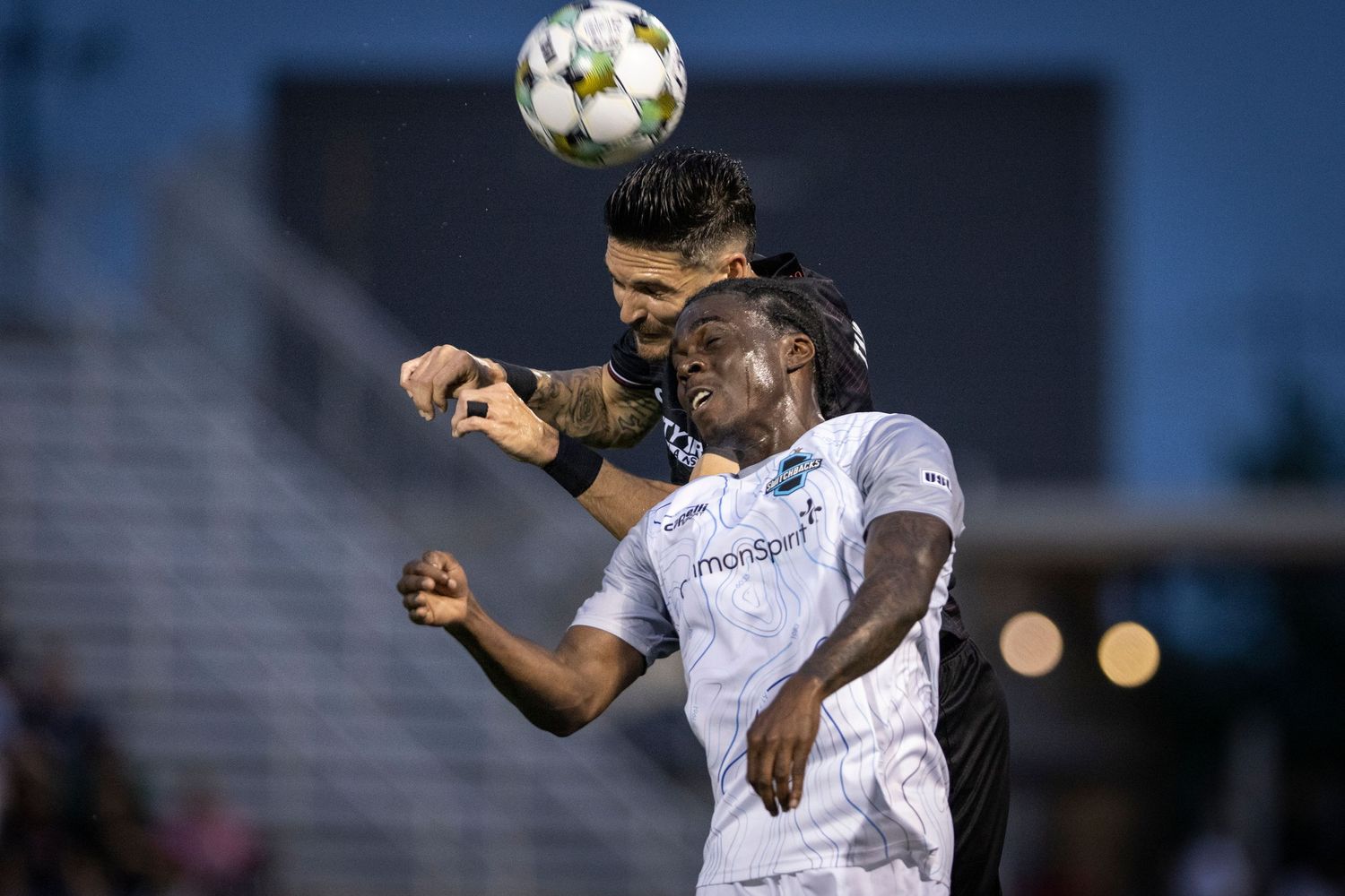 Two soccer players jump to head the ball during intense match action.