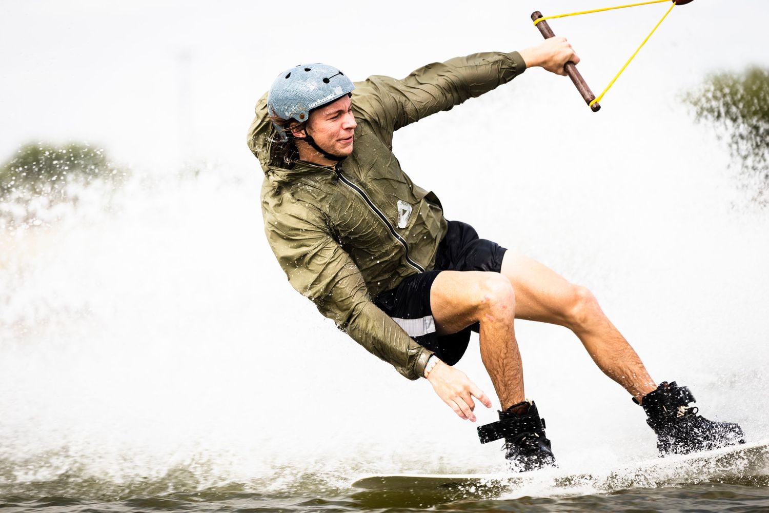 Wakeboarder in safety helmet performs aerial trick while jumping over wake on the water.