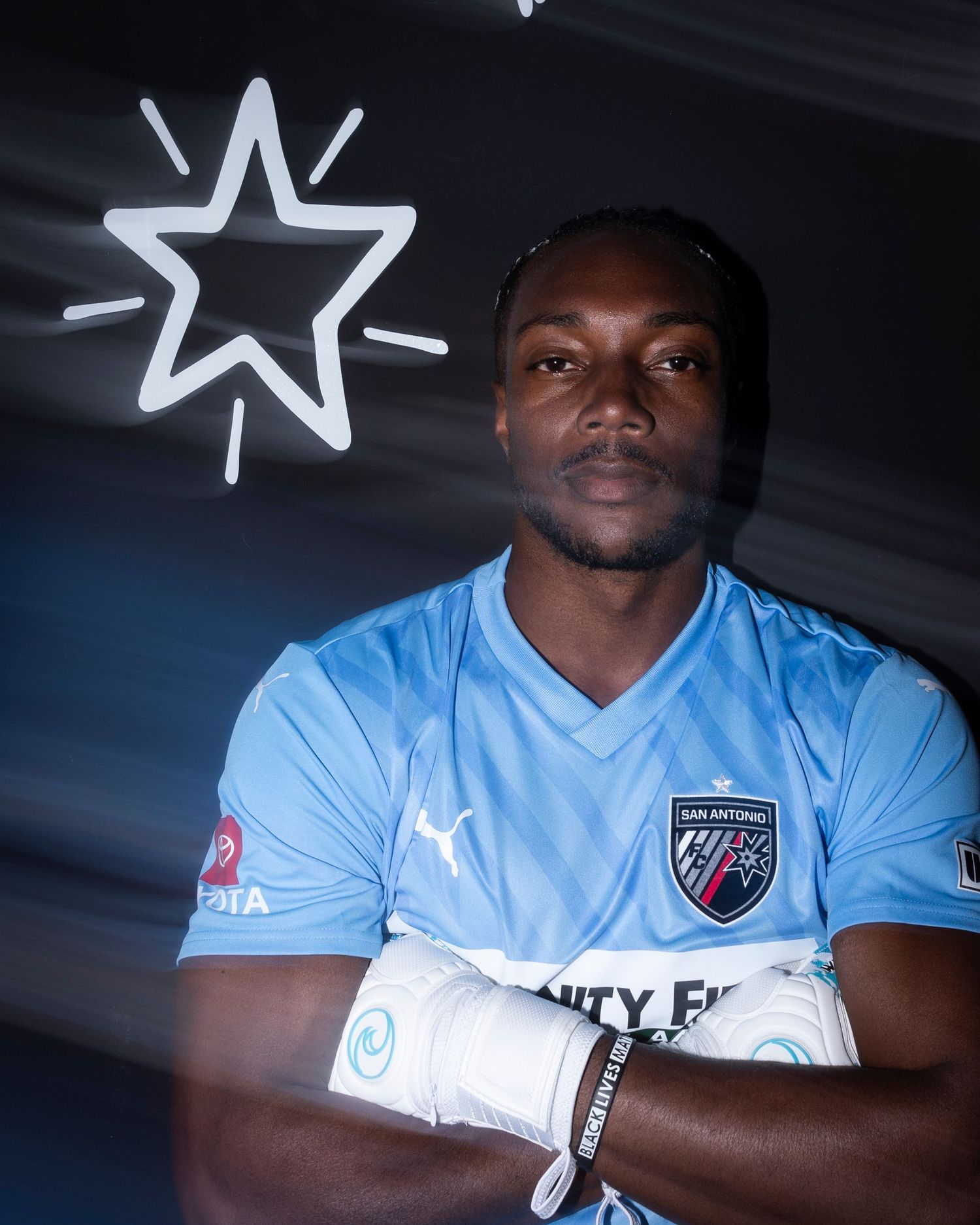 Soccer player in light blue jersey posing with neon star sign in background.