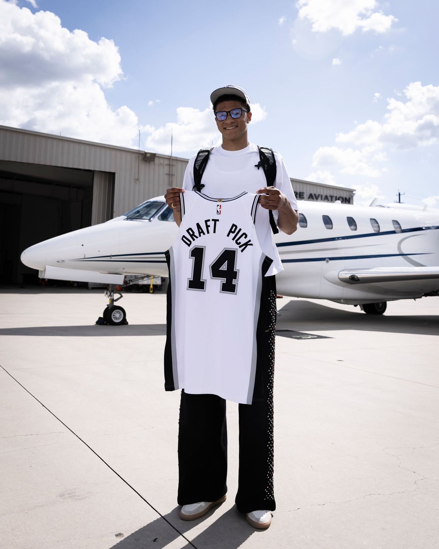 A basketball jersey with number 14 and 'PRATT' displayed in front of a private jet on an airport tarmac.