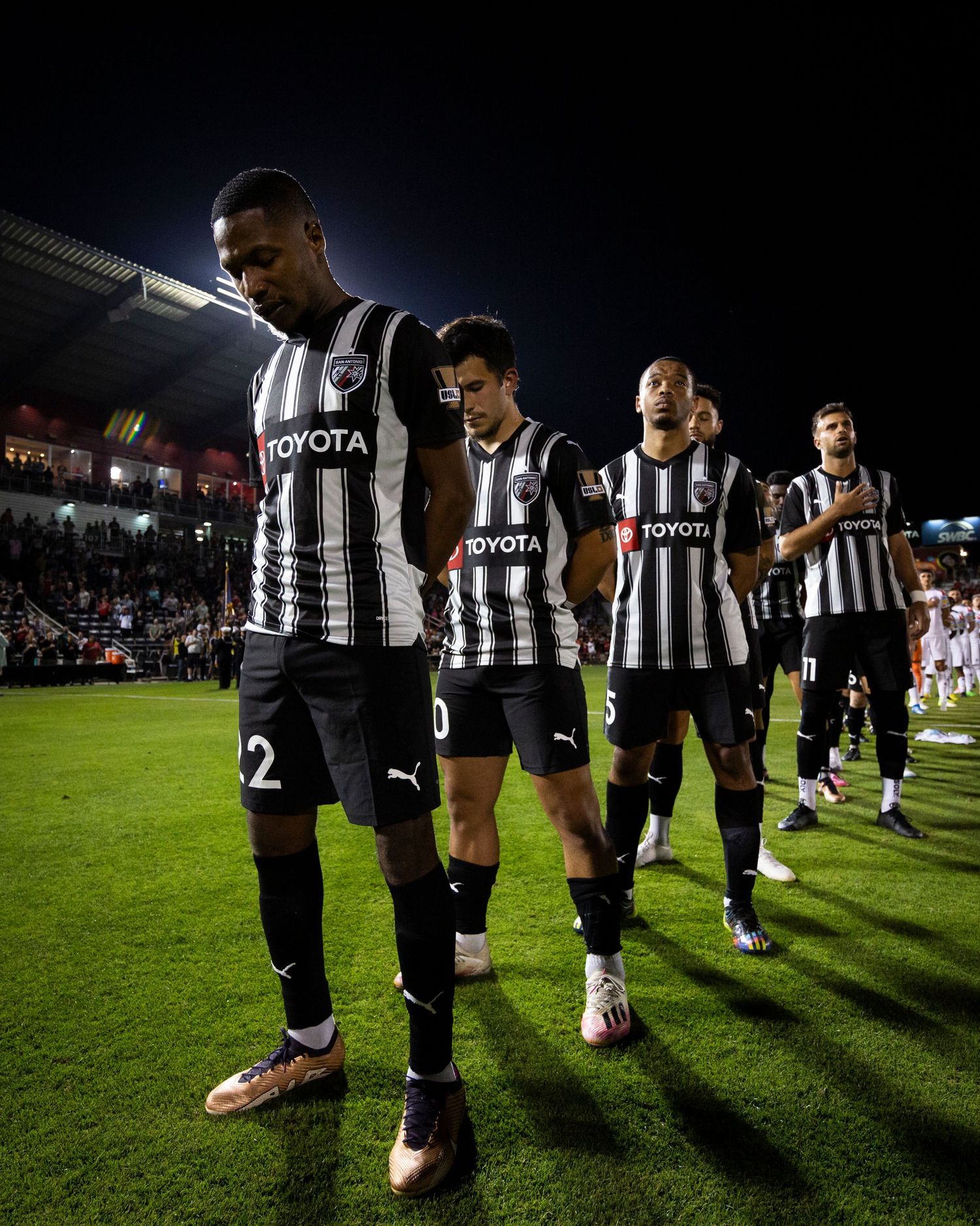 Soccer team in black and white striped uniforms walking together on field at night.