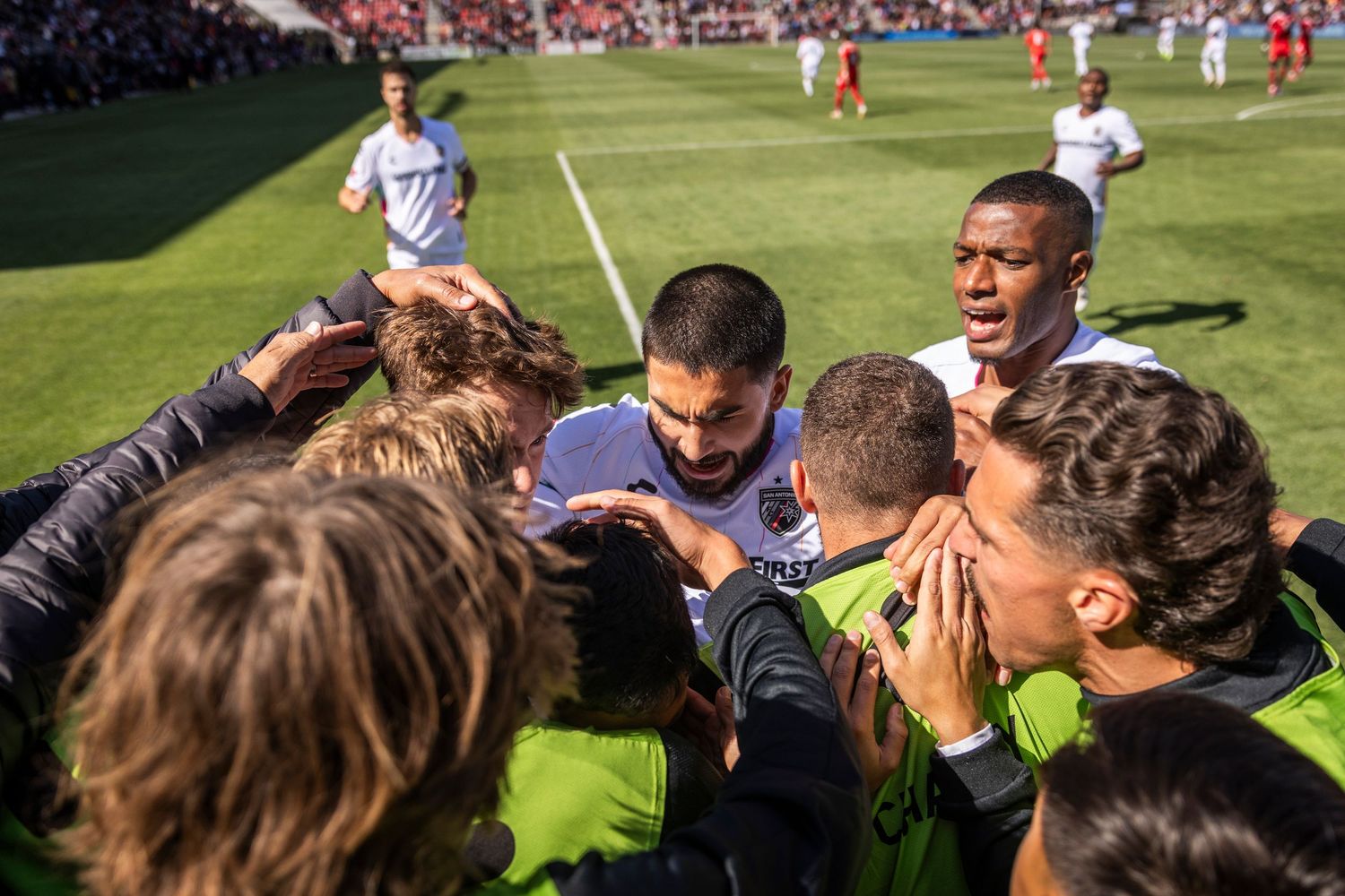 Soccer team huddles together on field during daytime match.