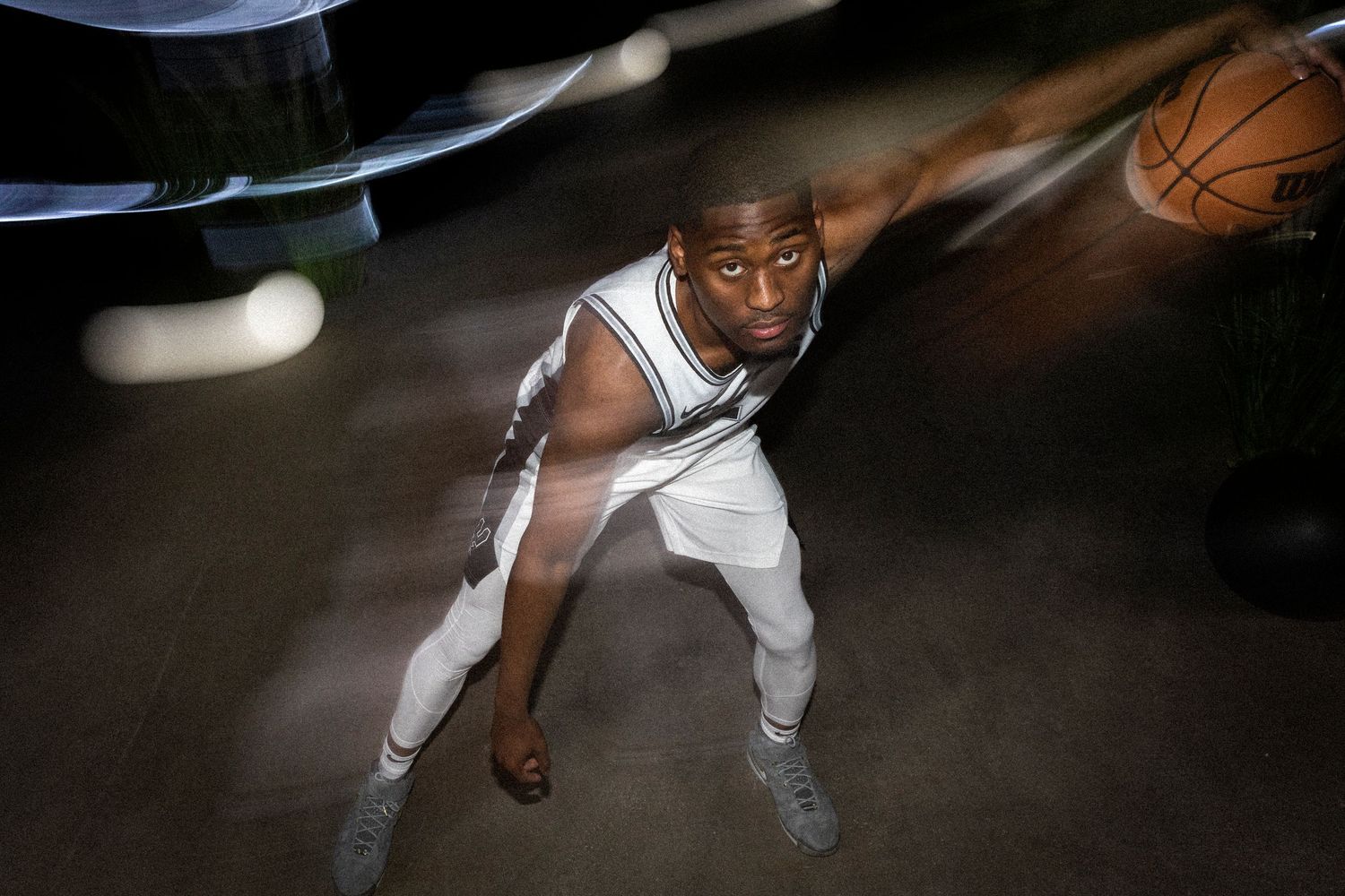 Basketball player in white uniform dribbling ball in dramatic lighting.