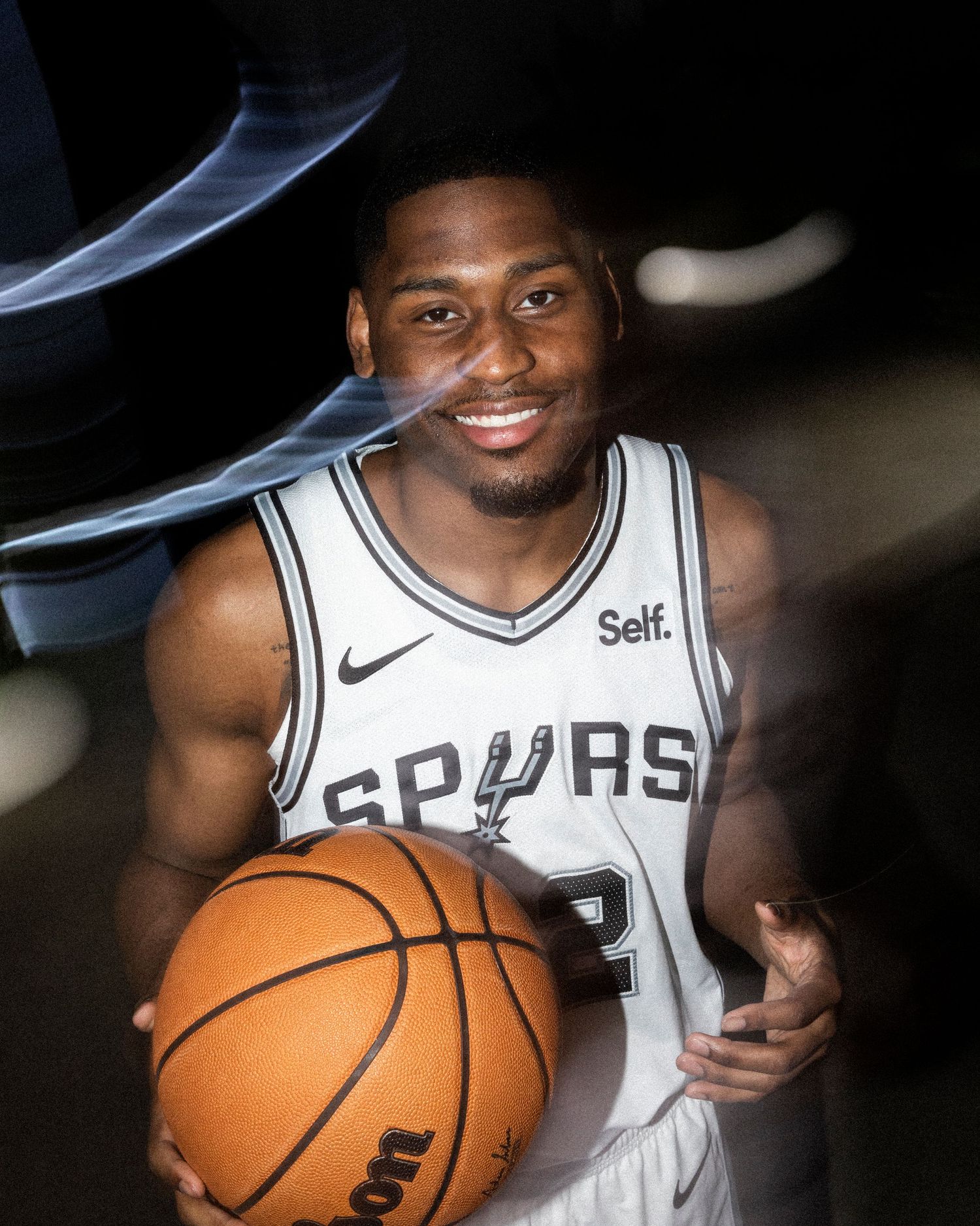 Basketball player in white Spurs jersey holding ball against dark background.
