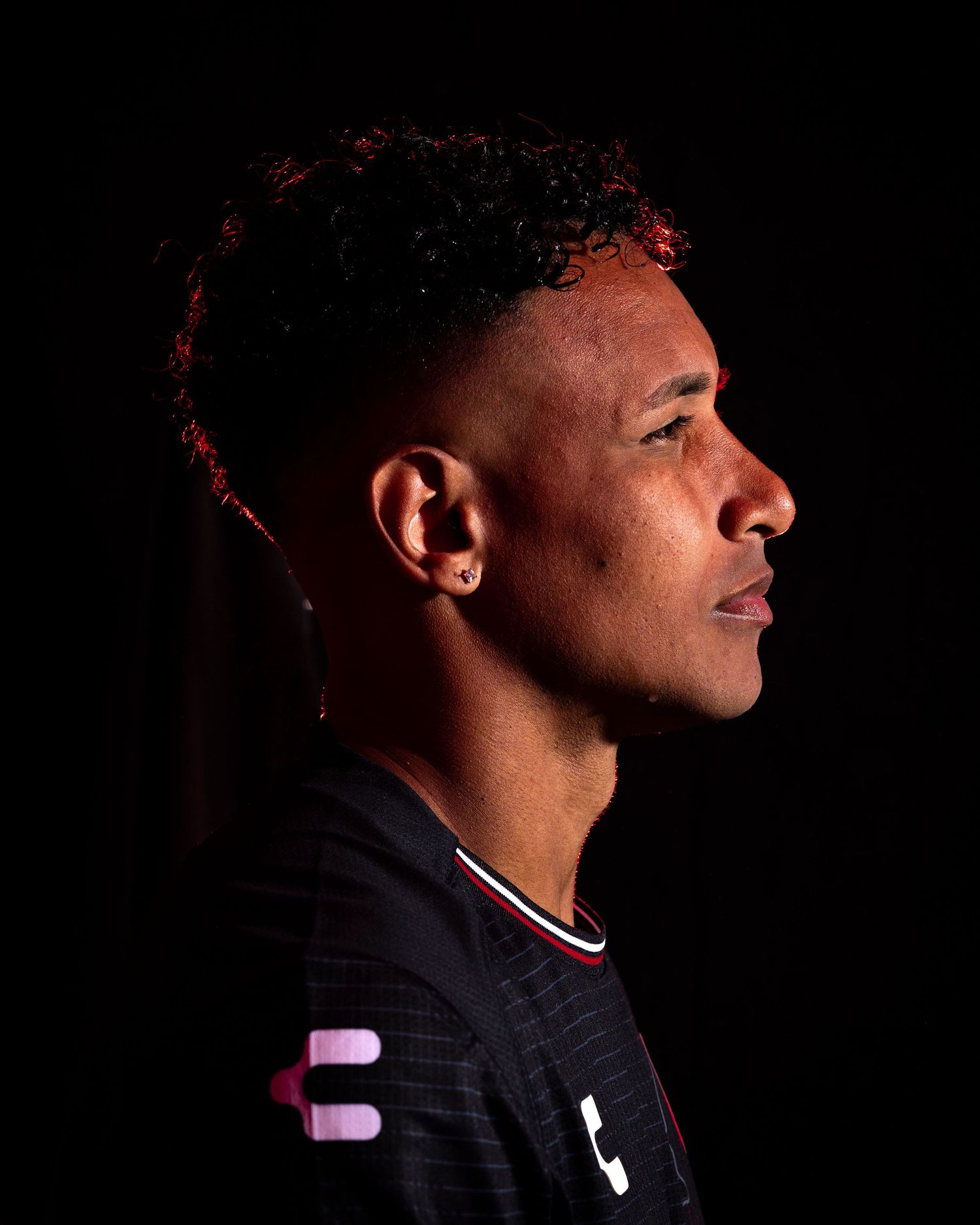 Athletic portrait with dramatic lighting showing side profile against dark background.