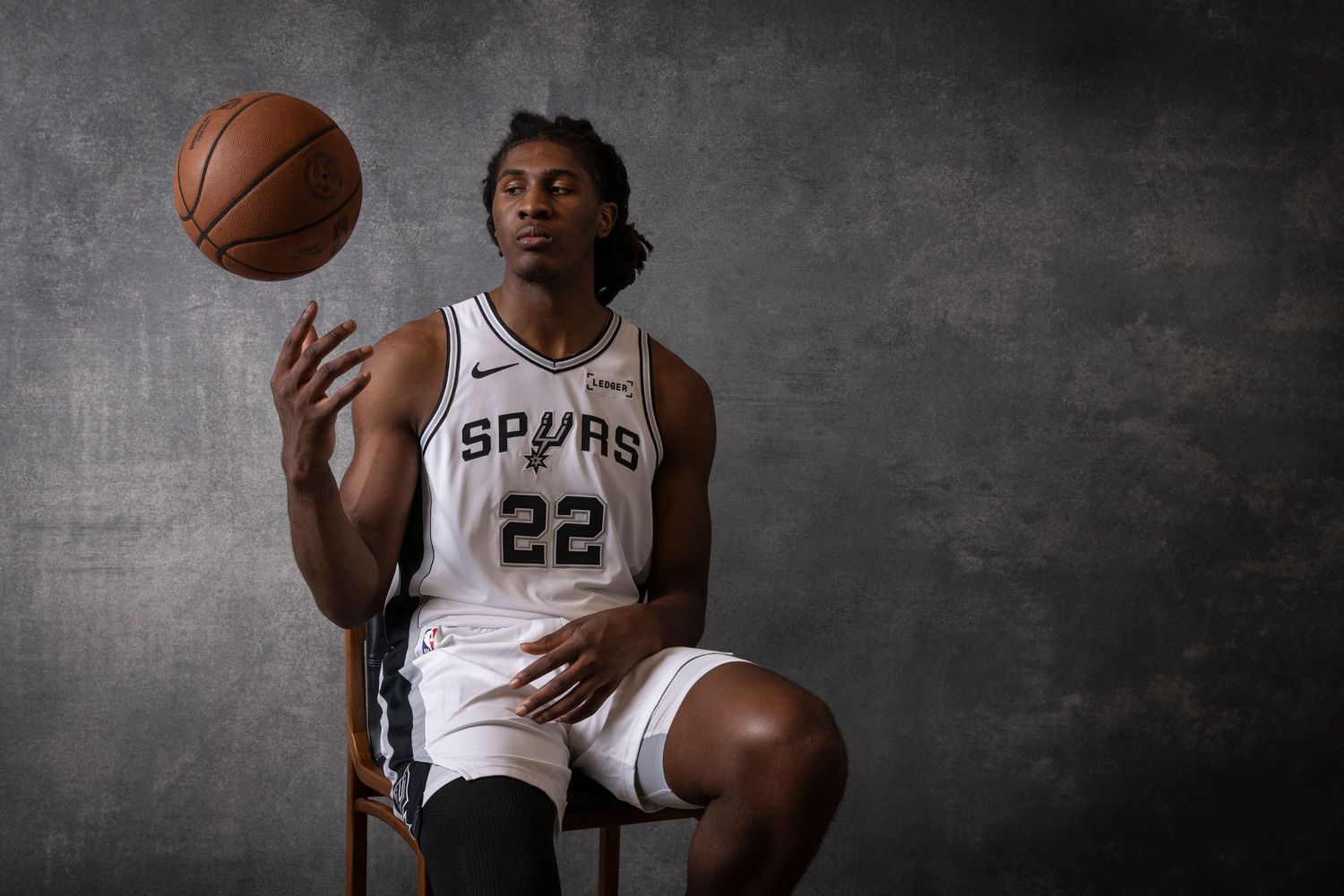 San Antonio Spurs player #22 sits on a chair spinning a basketball on his finger in a studio portrait.