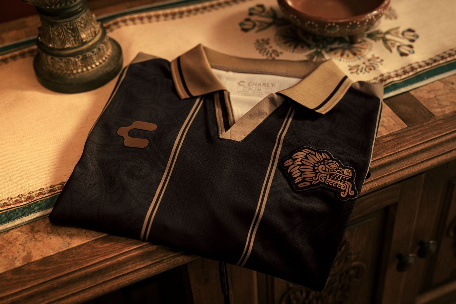 Black and gold Chicharo embroidered polo shirt folded on a wooden dresser.