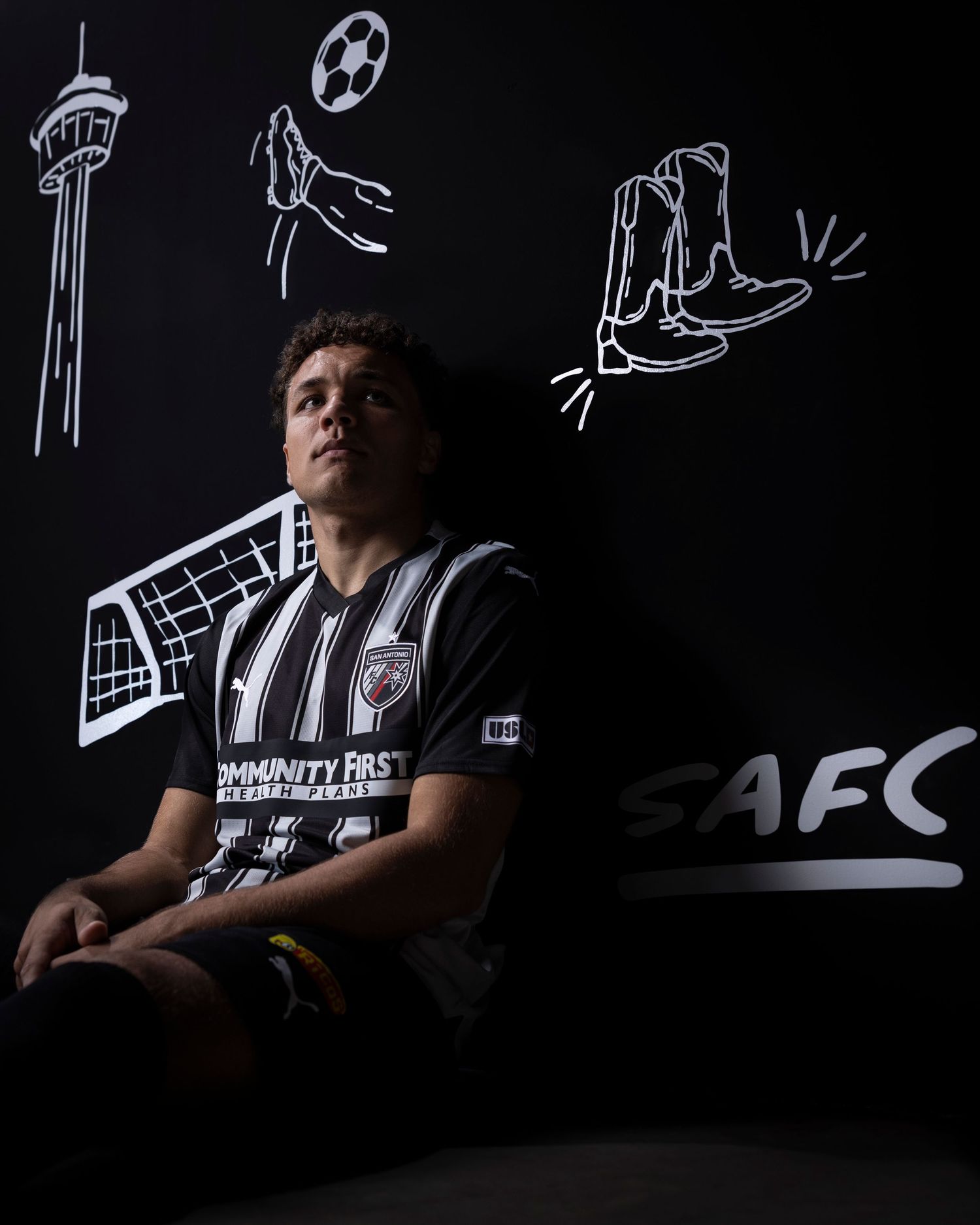 Player sits in dark setting with sports-themed chalk drawings on wall behind them.