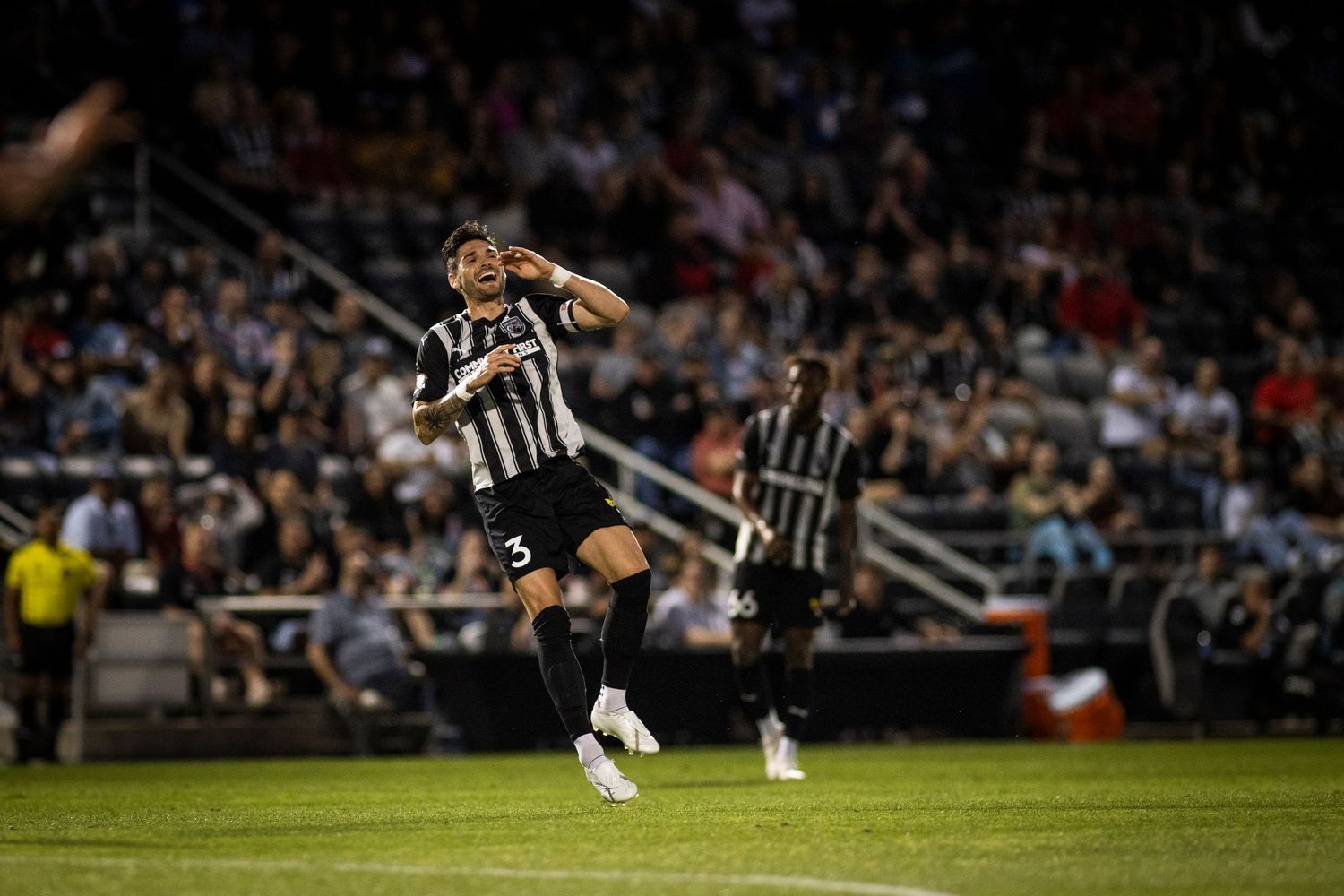 Soccer player in striped uniform leaps during nighttime match.