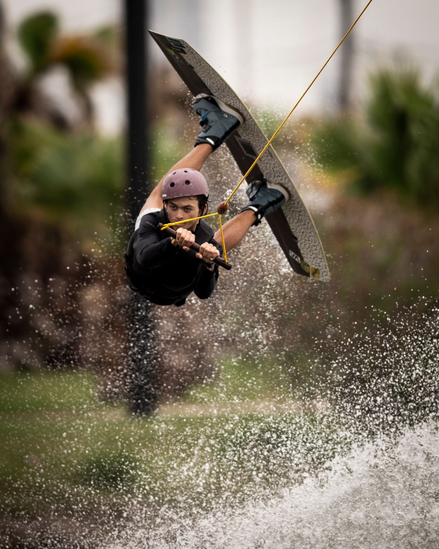 Wakeboarder performs an inverted aerial trick with dramatic water spray during a competition jump.