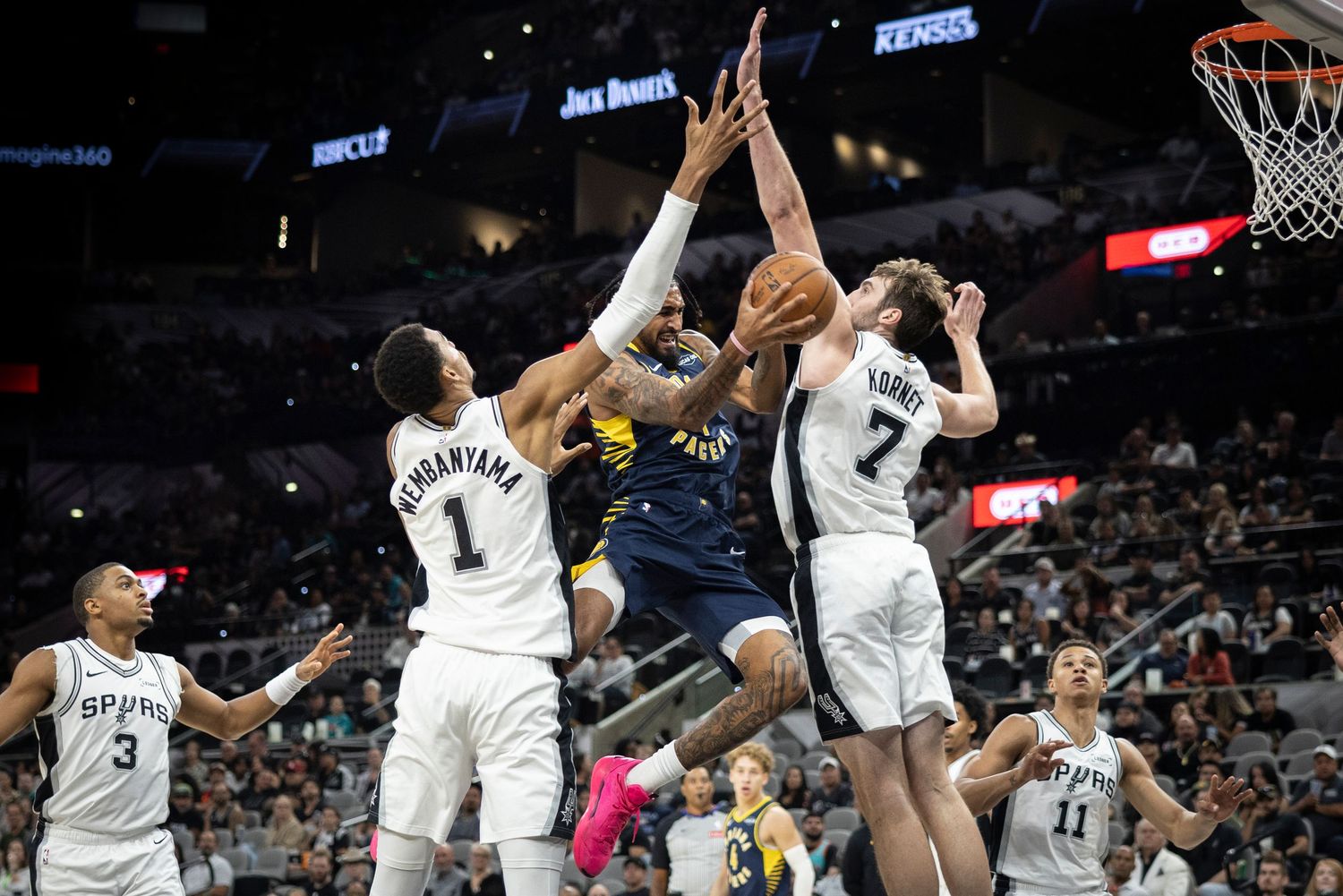 Professional basketball players jumping and contesting for the ball near the hoop during a game.