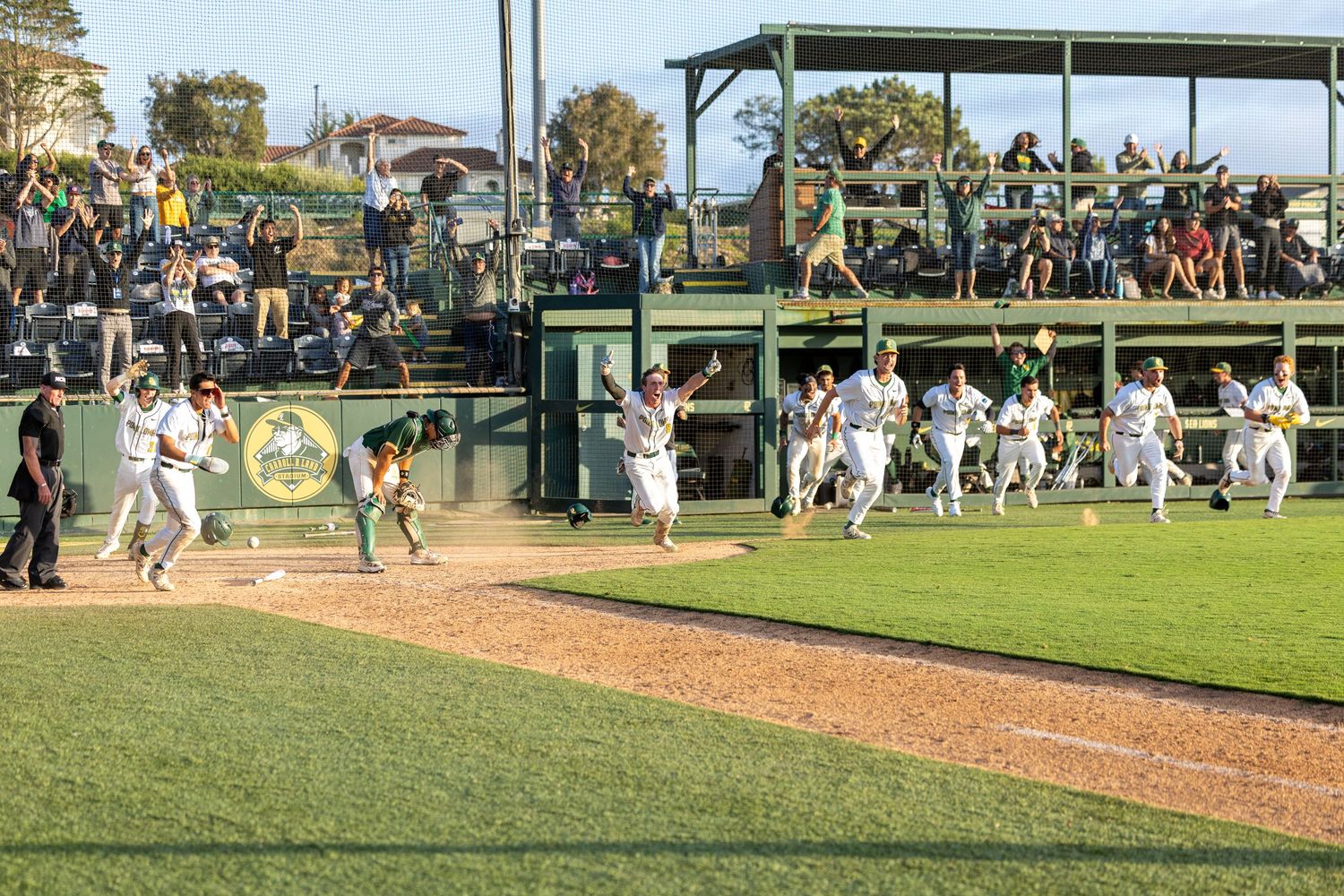 Baseball players in white uniforms sprint across the infield toward teammates to celebrate as fans watch from the stands on a sunny day.