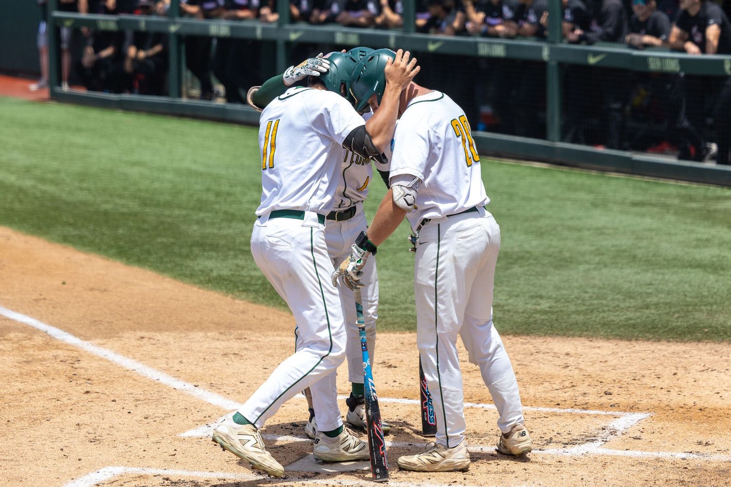 Two baseball players in white uniforms and a green helmet celebrate at home plate with a chest bump on a sunny day.