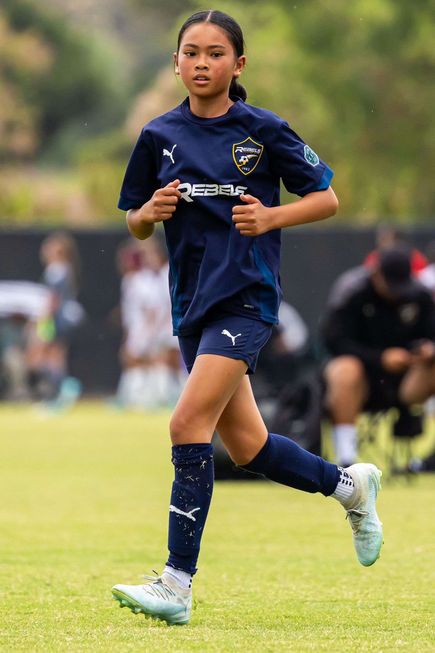 Soccer player in navy blue Puma uniform runs on grass field during match.