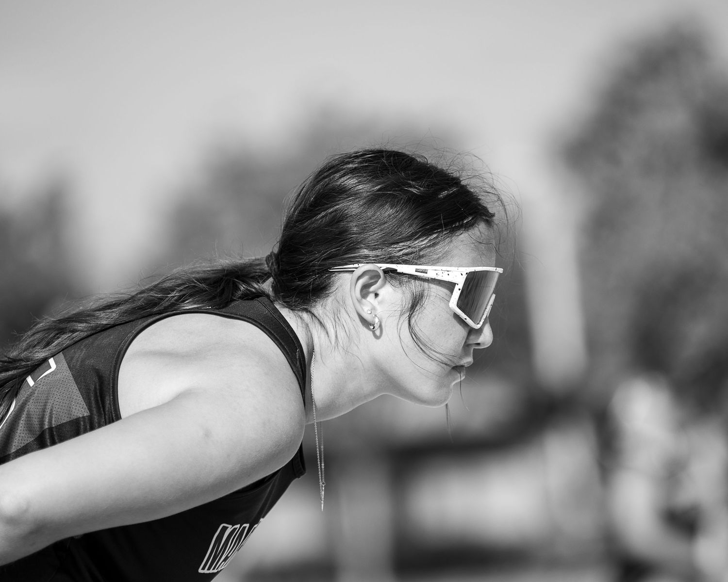 Black and white photo of a female athlete wearing sunglasses and a sleeveless top, leaning forward mid-race.