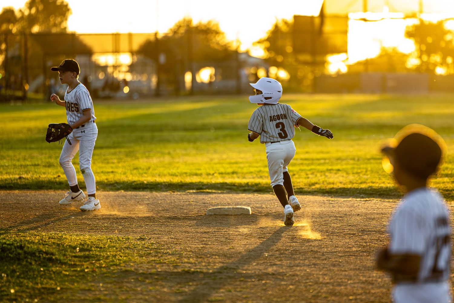 Baseball players practicing during golden hour with long shadows on the field.