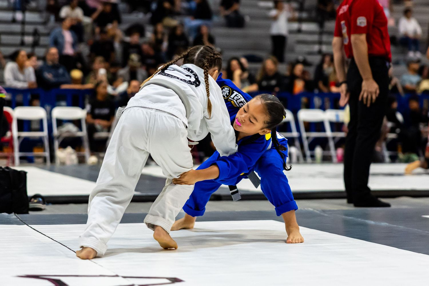 Two jiu-jitsu competitors grapple on mat during tournament match.