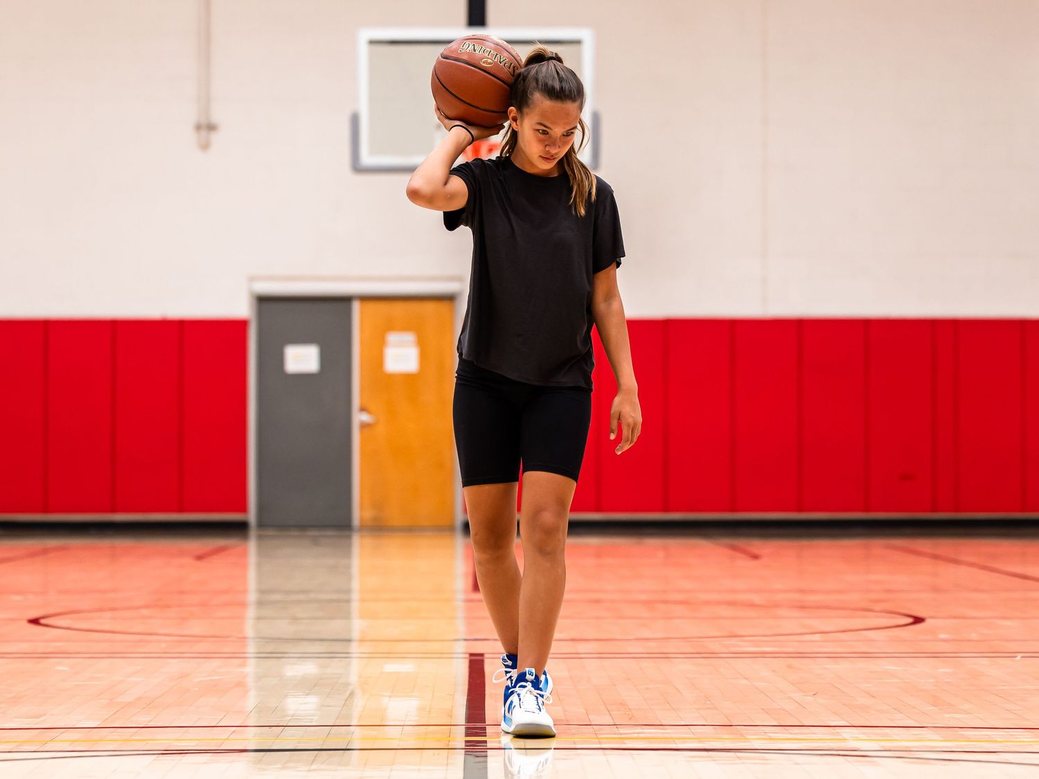 Basketball player dribbling on indoor court with red walls and white trim.